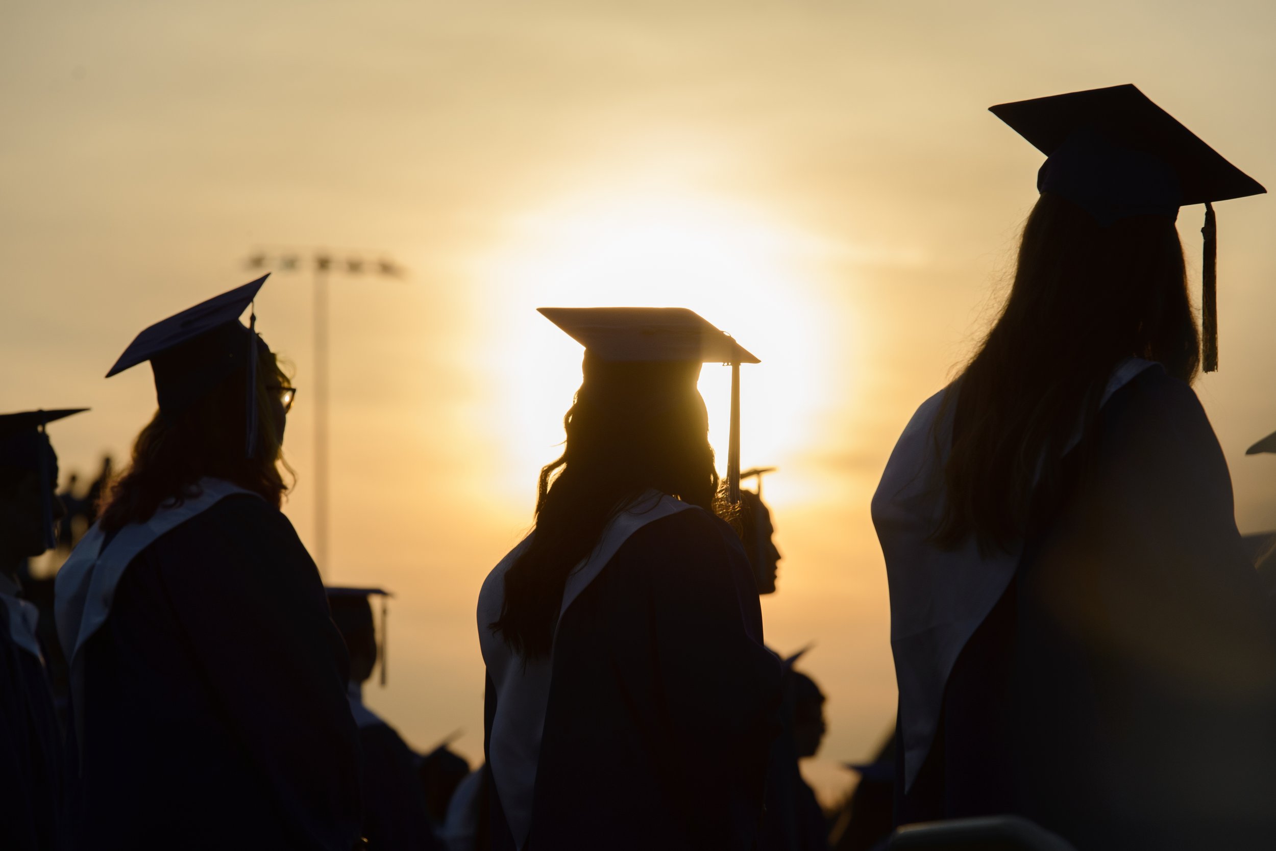  Graduates are silhouetted by the setting sun during graduation on Friday, May 21, 2021 at Oconee County High School in Watkinsville, Georgia. Oconee County High School hosted its graduation outdoors in Warrior Stadium. (Julian Alexander for the Athe