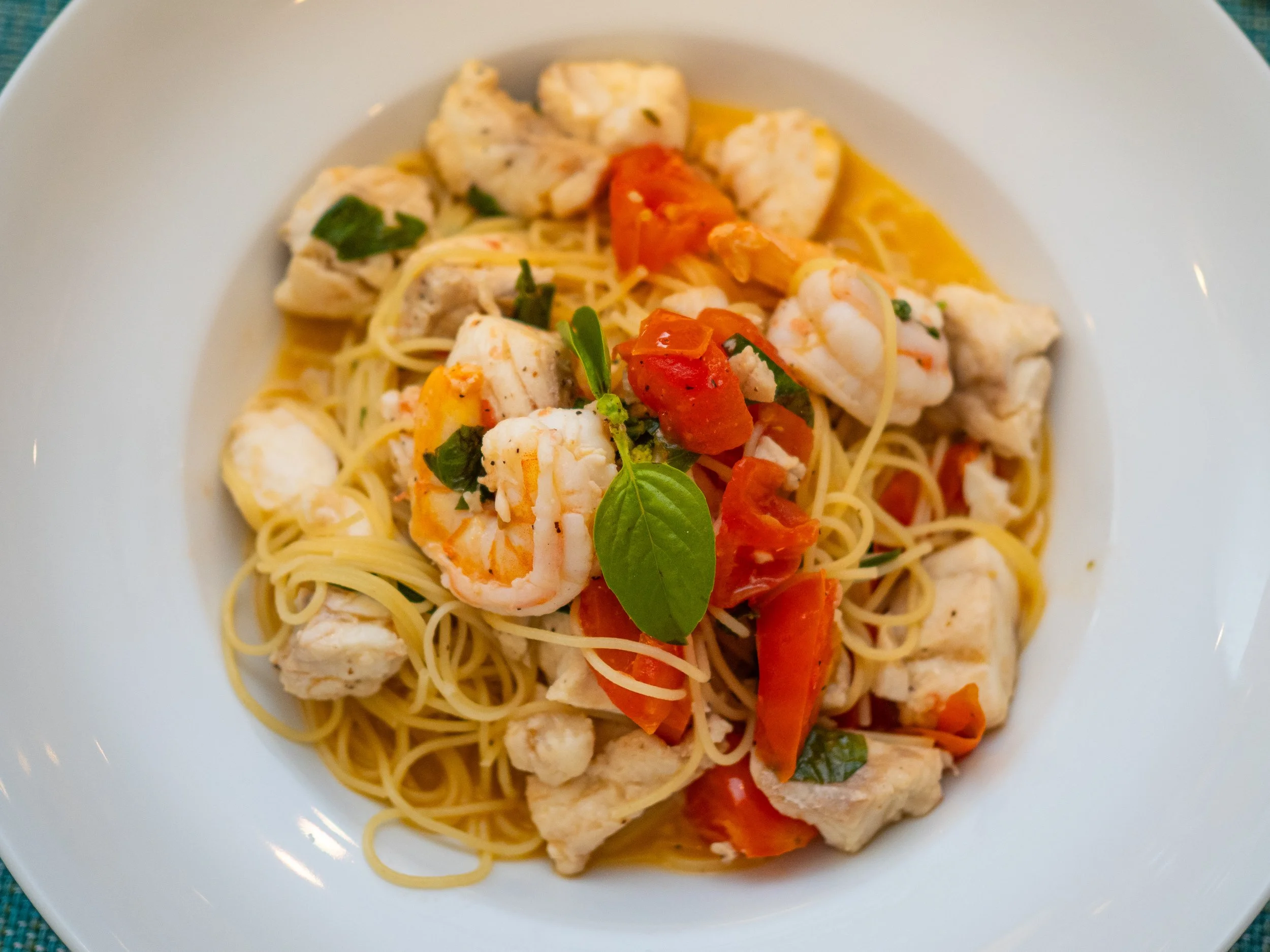 A fresh seafood pasta dish at Red Ginger in San Pedro, Belize, featuring local shrimp, white fish, and cherry tomatoes over linguine with a fresh basil garnish.