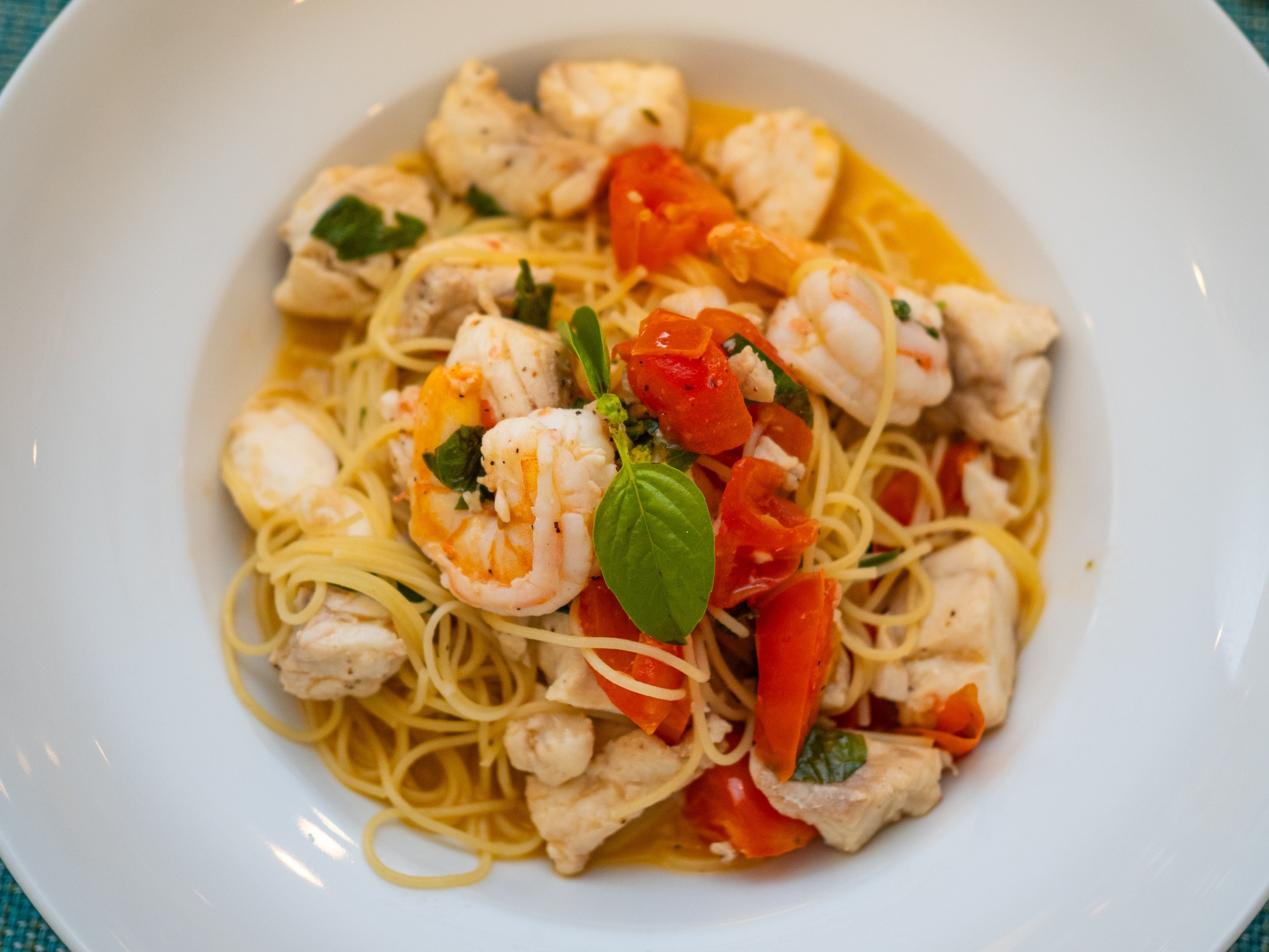 A fresh seafood pasta dish at Red Ginger in San Pedro, Belize, featuring shrimp, locally sourced fish, and cherry tomatoes over linguine, garnished with fresh basil on Front Street.