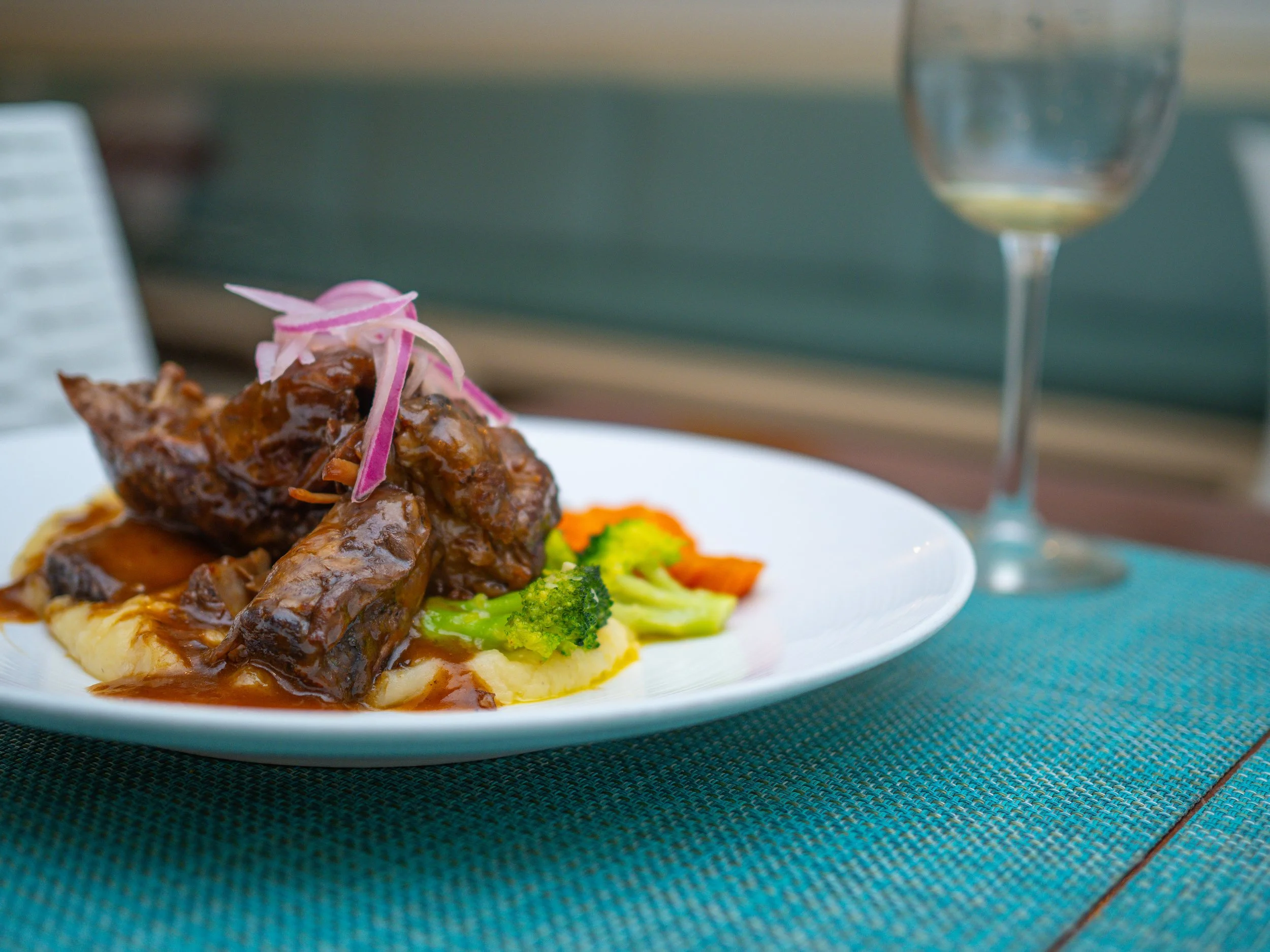 A gourmet braised short rib dish served with seasonal vegetables and a glass of white wine at Red Ginger restaurant in San Pedro, Belize.