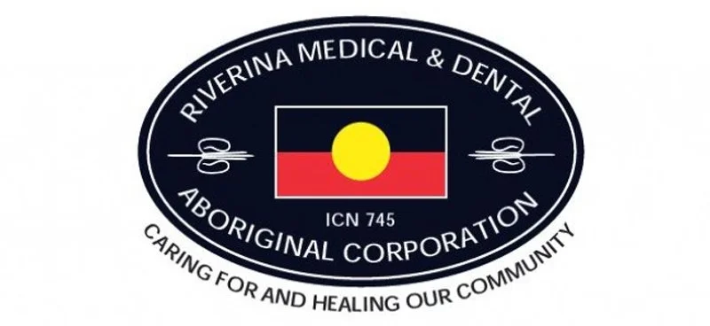 Logo of Riverina Medical & Dental Aboriginal Corporation featuring an oval design with black background, white text, a flag with a yellow circle, black, red, and yellow colors, and scissors symbol.
