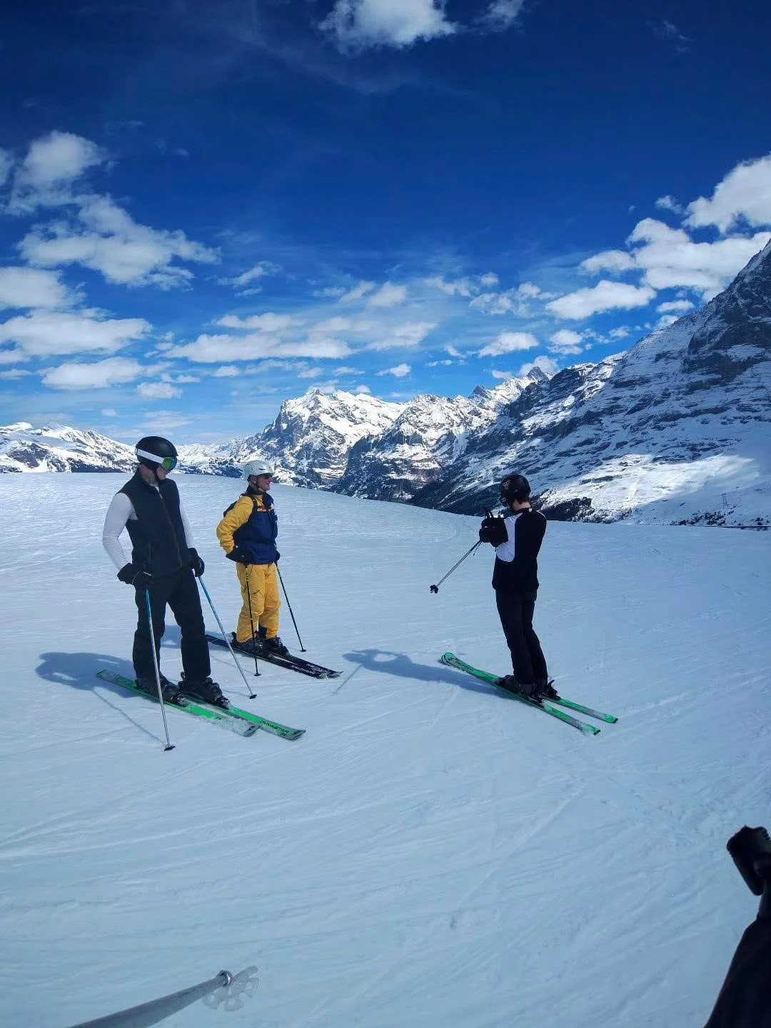 Three young people in ski equipment stand on a slope with beautiful mountains in the distance