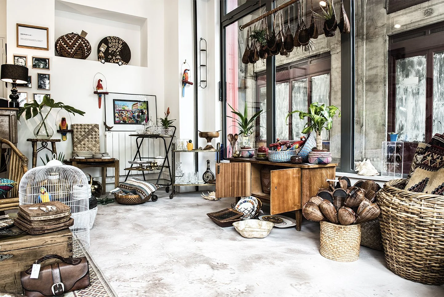 Ma boutique d'antiquités remplie d'objets en rotin, vases, paniers, et déco colorée, avec grandes fenêtres laissant entrer la lumière naturelle.