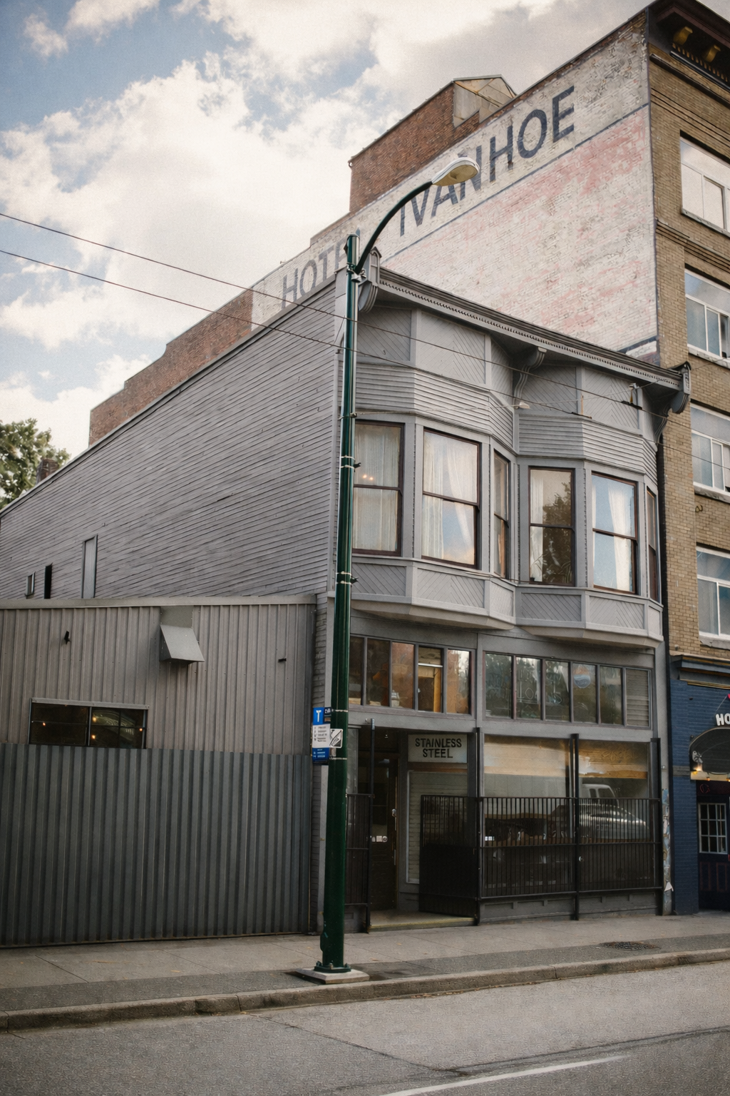 A multi-story building with a faded sign that reads 'HOTEL VAN HOOE' on the top brick wall, cloudy sky, streetlamp in front, and street-level glass and metal storefront.