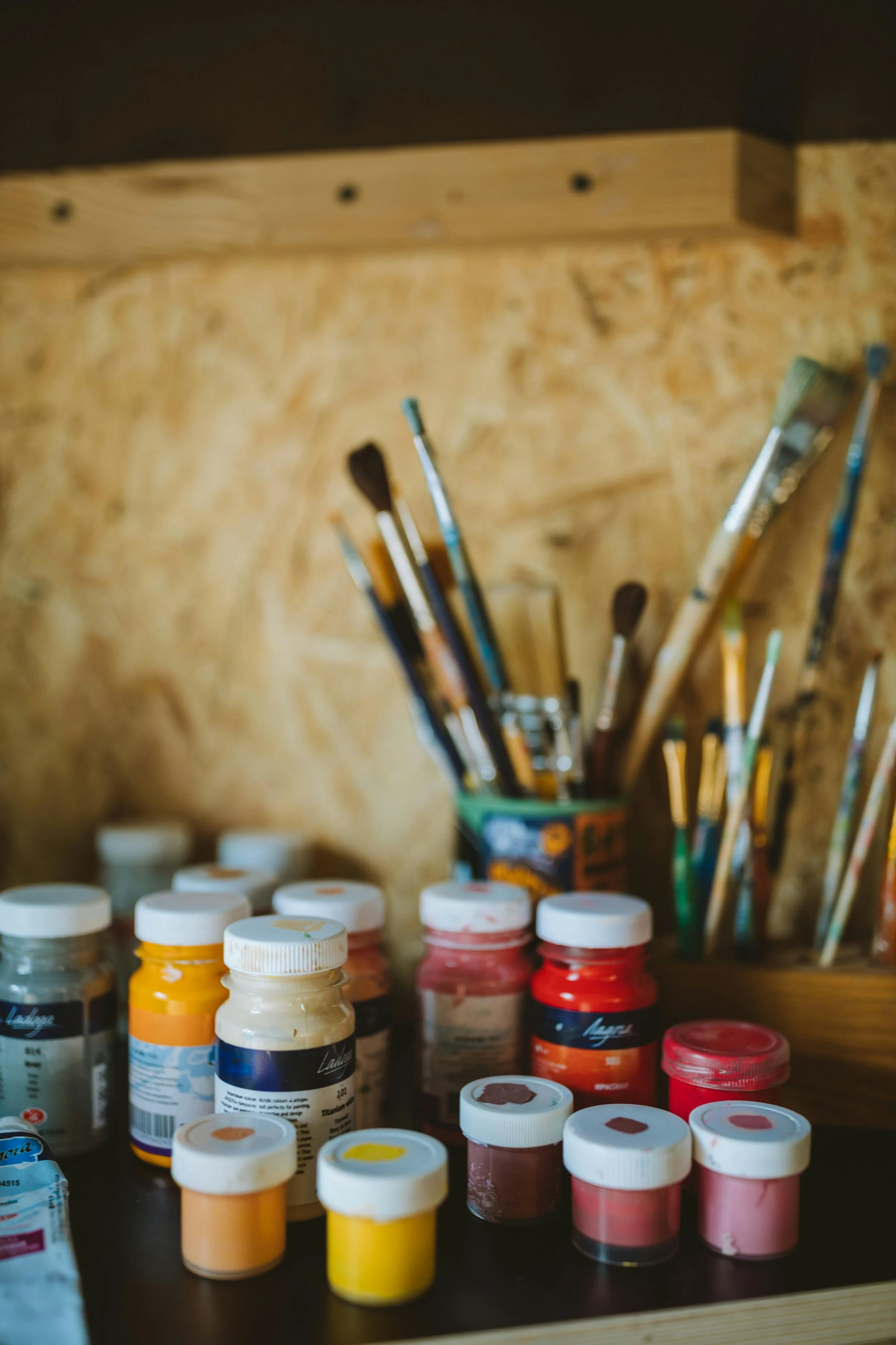 A collection of paint jars and paintbrushes in a wooden container on a worktable