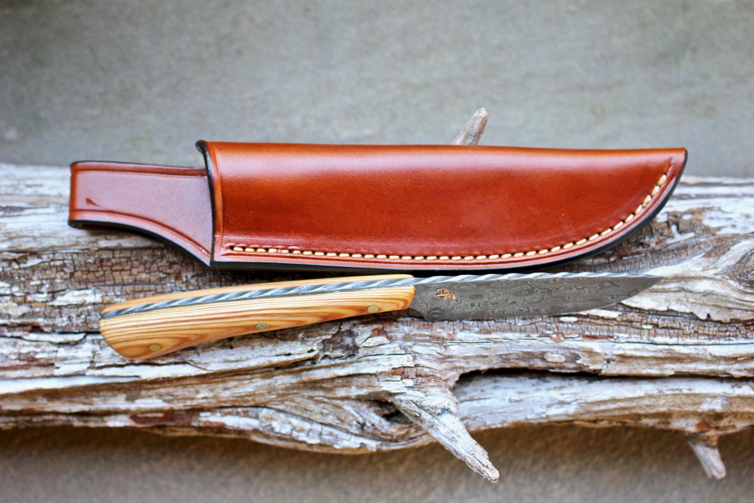 I recently finished this “knife set” for a client and now friend. The field knife was hand forged from 1095/15N20 “raindrop” pattern welded damascus. The blade is 2 15/16” long with an overall length of 7 13/16”. Along the entire spine is “twisted rope” hand filework. It has peened brass pins and a central “dog paw” mosaic pin. The handles to both are made from stabilized old growth Pine that came from a family barn in Deepstep, GA built in 1926 and has a lot of sentimental value to the owner. The sheath is by Upland Custom Leather. The oyster knife was also hand forged, but from 5160 HCS with a 2 2/4” blade and total length of 6 11/16” and has the same configuration. Pine may be soft but it sure can be pretty. Despite the wood being 92+ years old, when I worked it you would have thought I had opened a bottle of Pine-Sol.