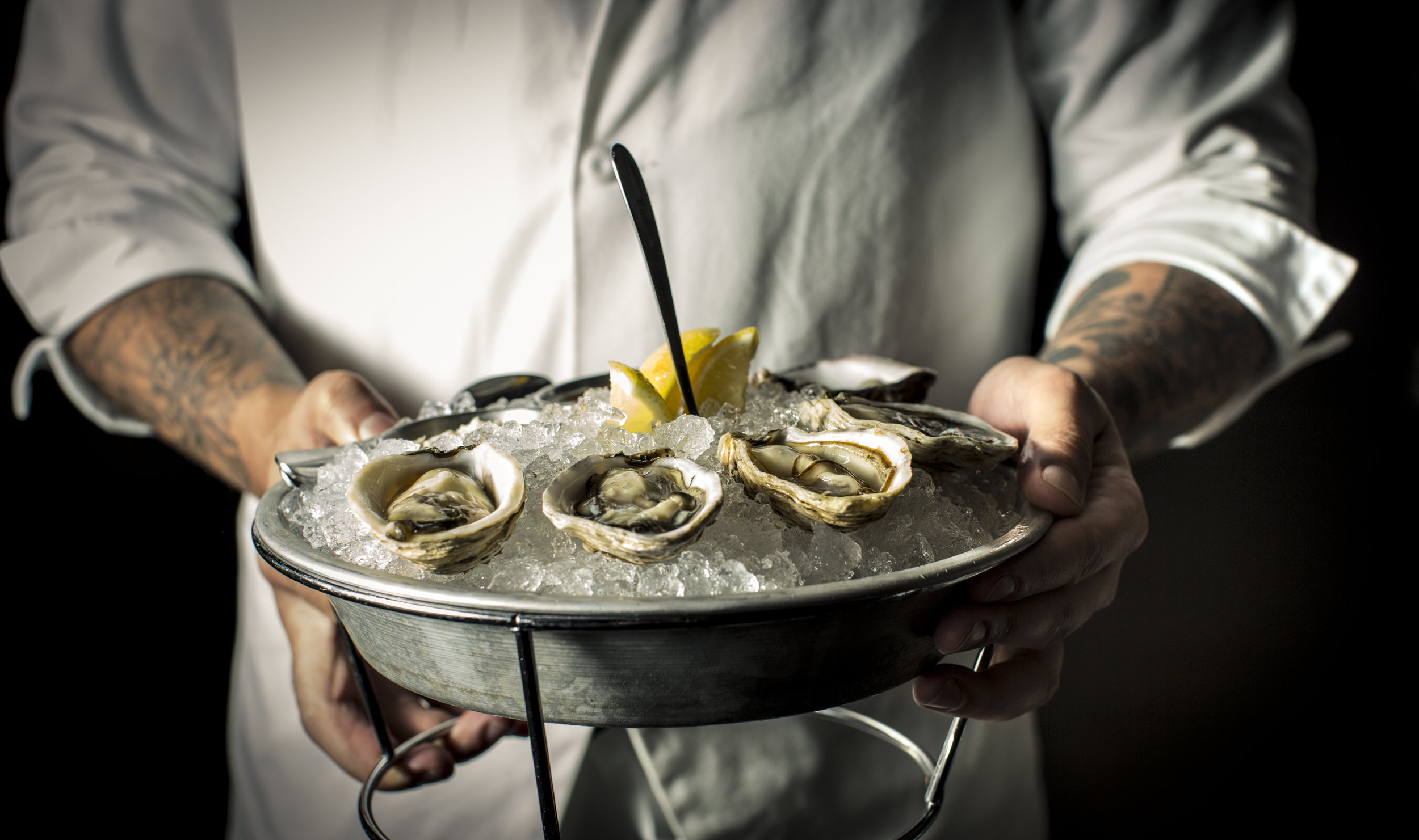  Chef holding a platter of shucked raw oysters over bed of ice 