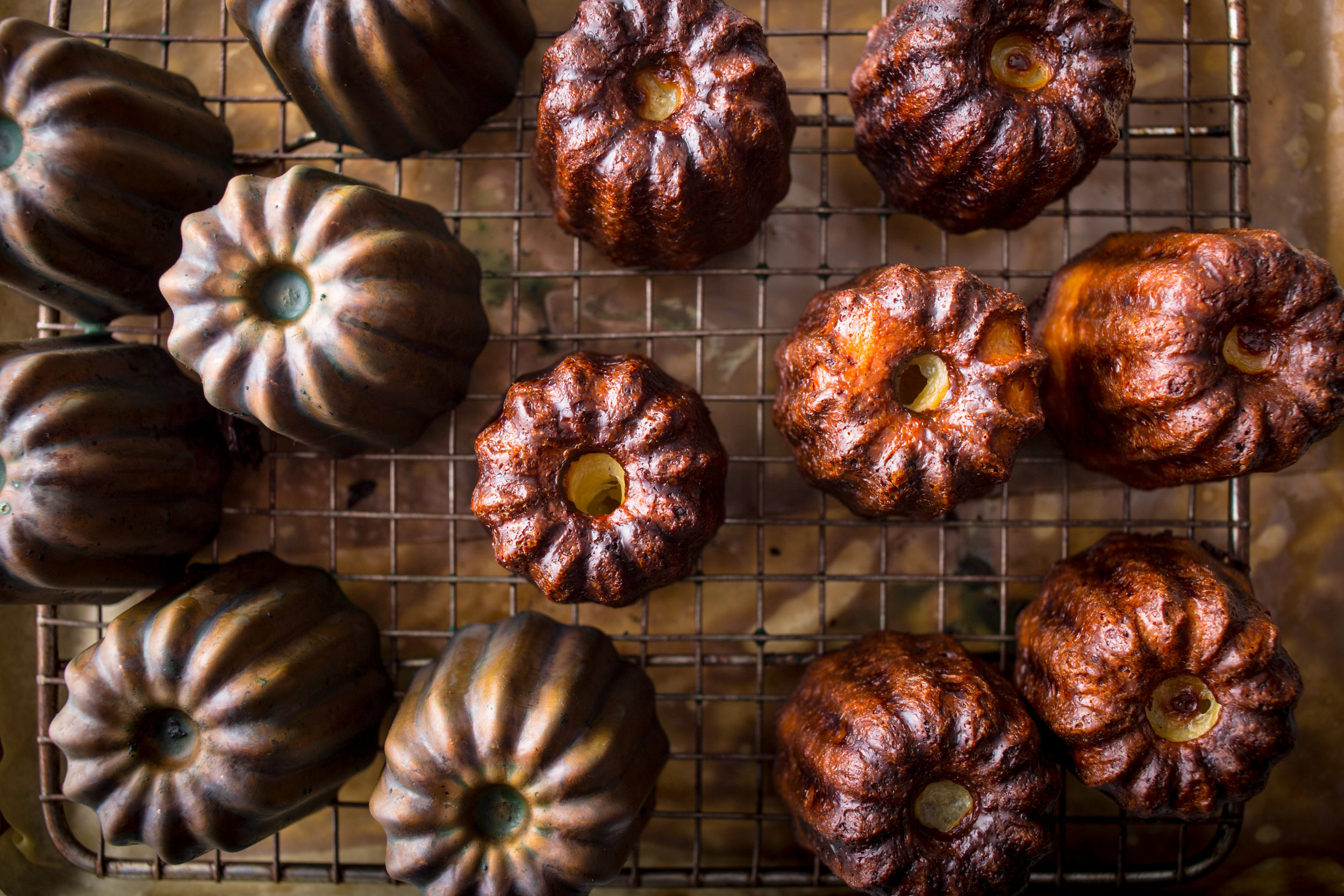  baked canelés resting on wire rack next to metal canelé molds 