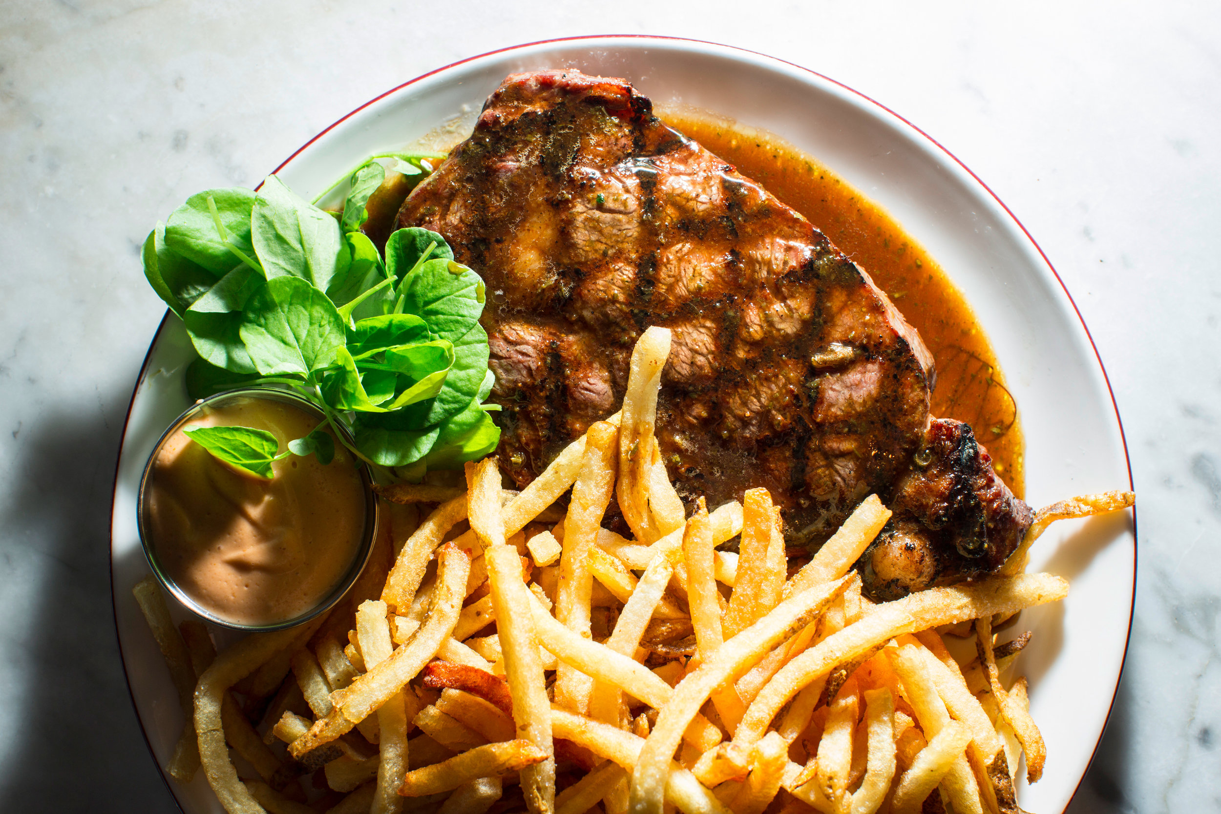  Plate of grilled steak with small ramekin of sauce, lettuce garnish and large pile of french fries 