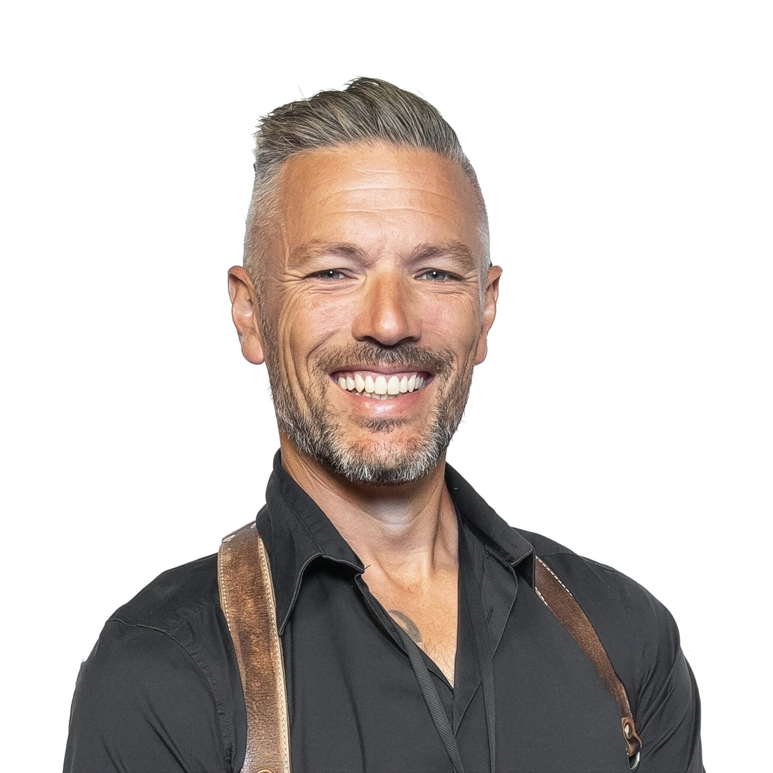 Close-up of a smiling middle-aged man with short gray hair, facial hair, and a tan leather strap on his shoulder against a white background.