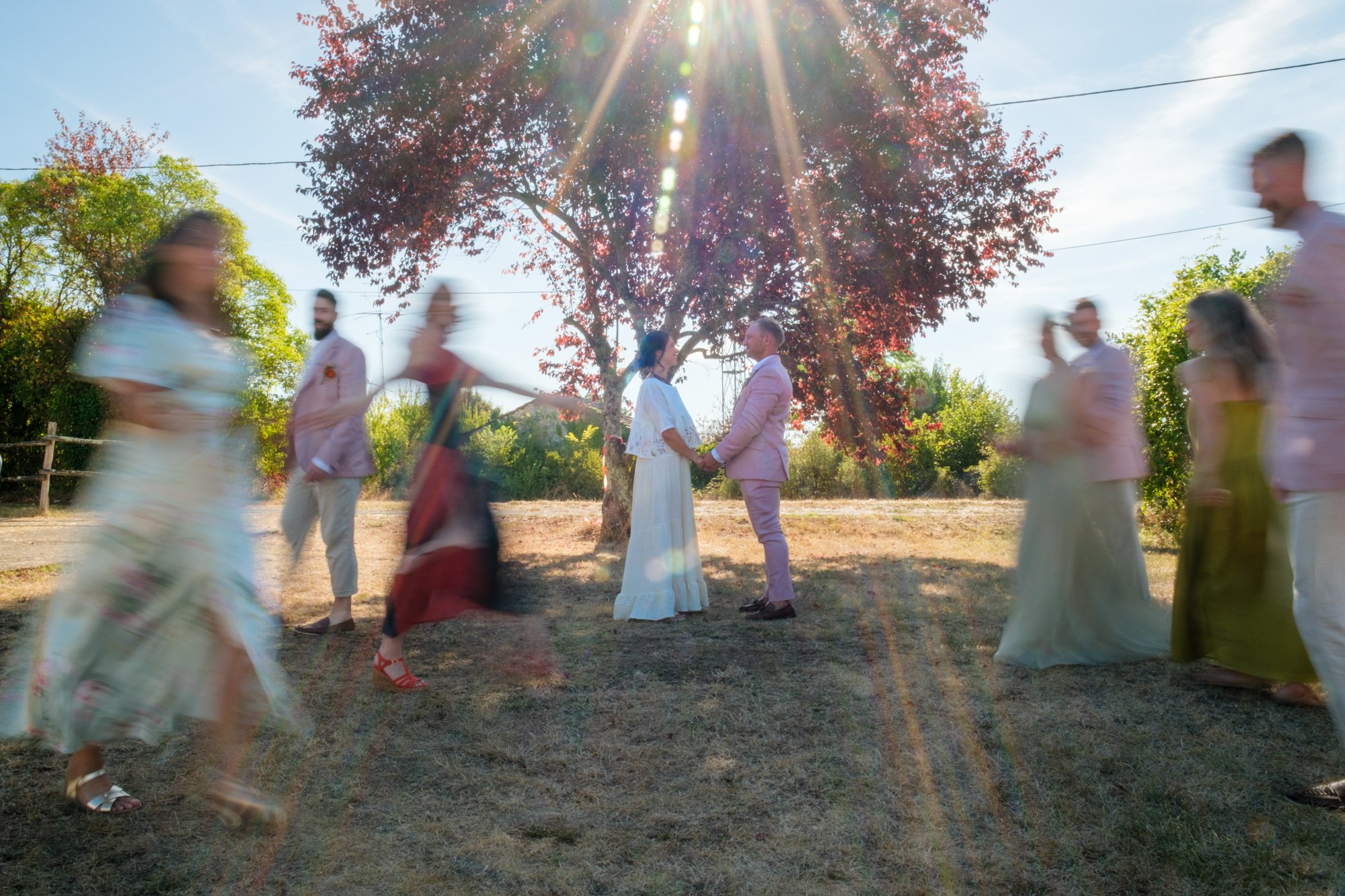 Bride and groom standing still holding hand whilst their wedding party walk past them creating a blur