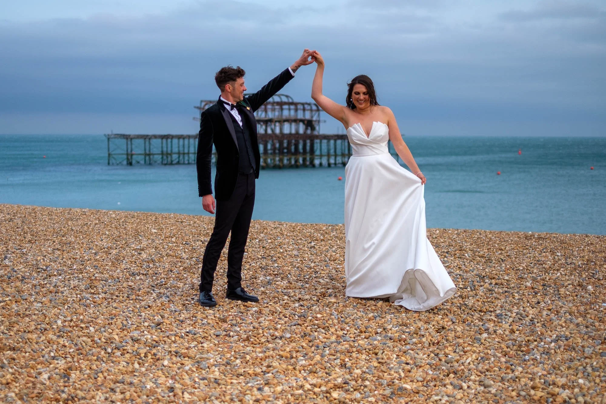 A bride and groom dancing on a Brighton beach with the sea and the old west pier in the background.