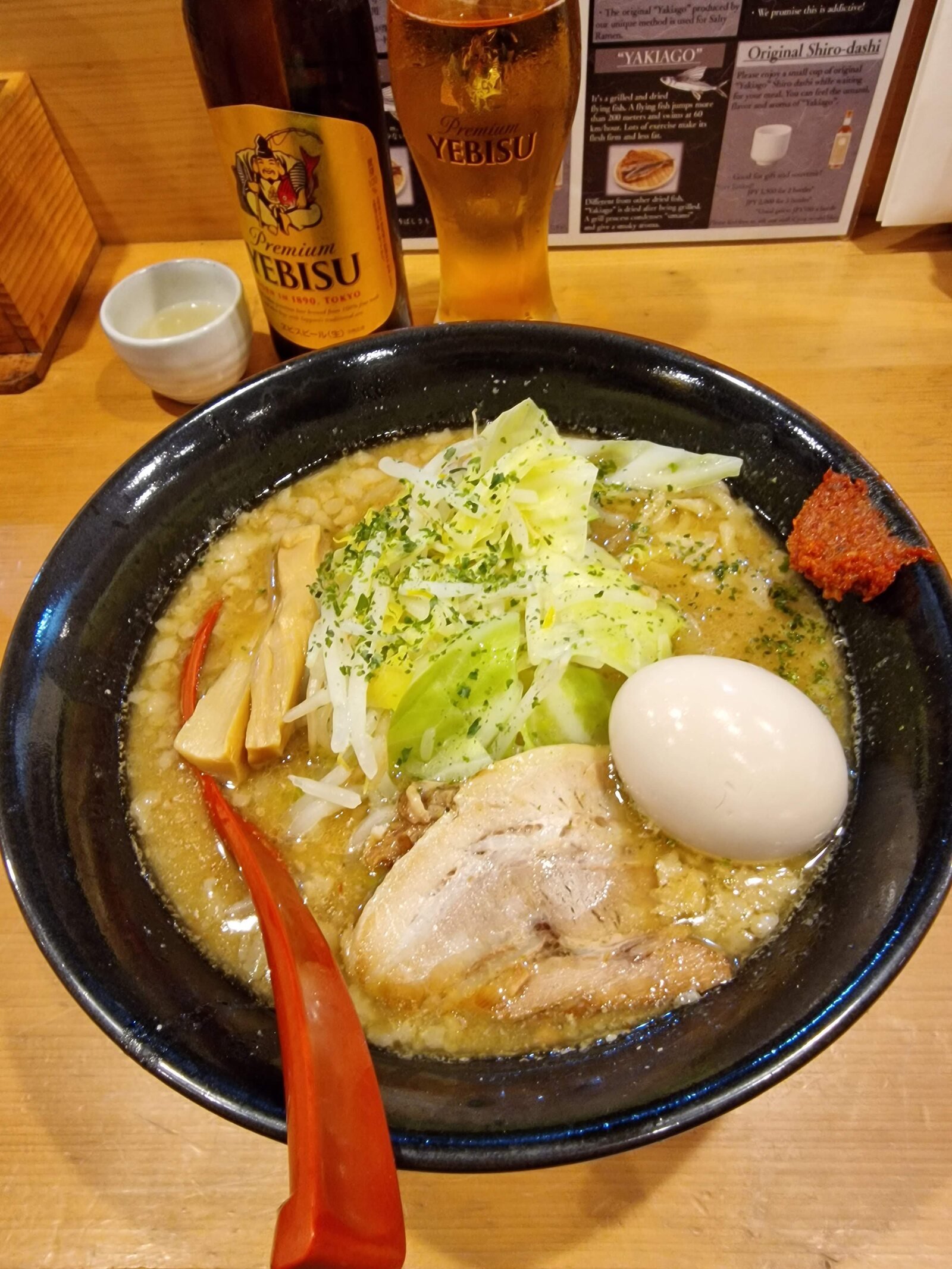 a black bowl full of ramen, meat, an egg and salad with a red spoon in it