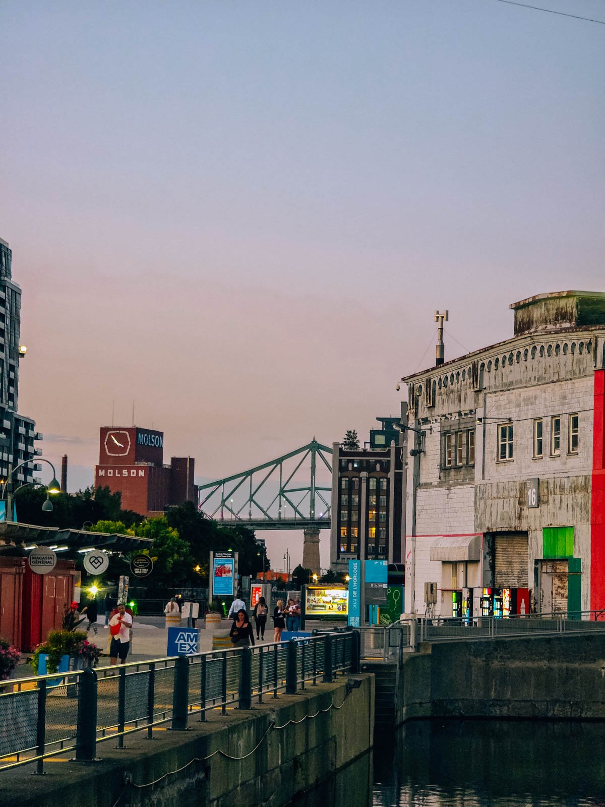 Looking across the Old Port of montreal with many old port buildings, industrial buildings, a bridge and an old brewery visiible at dusk