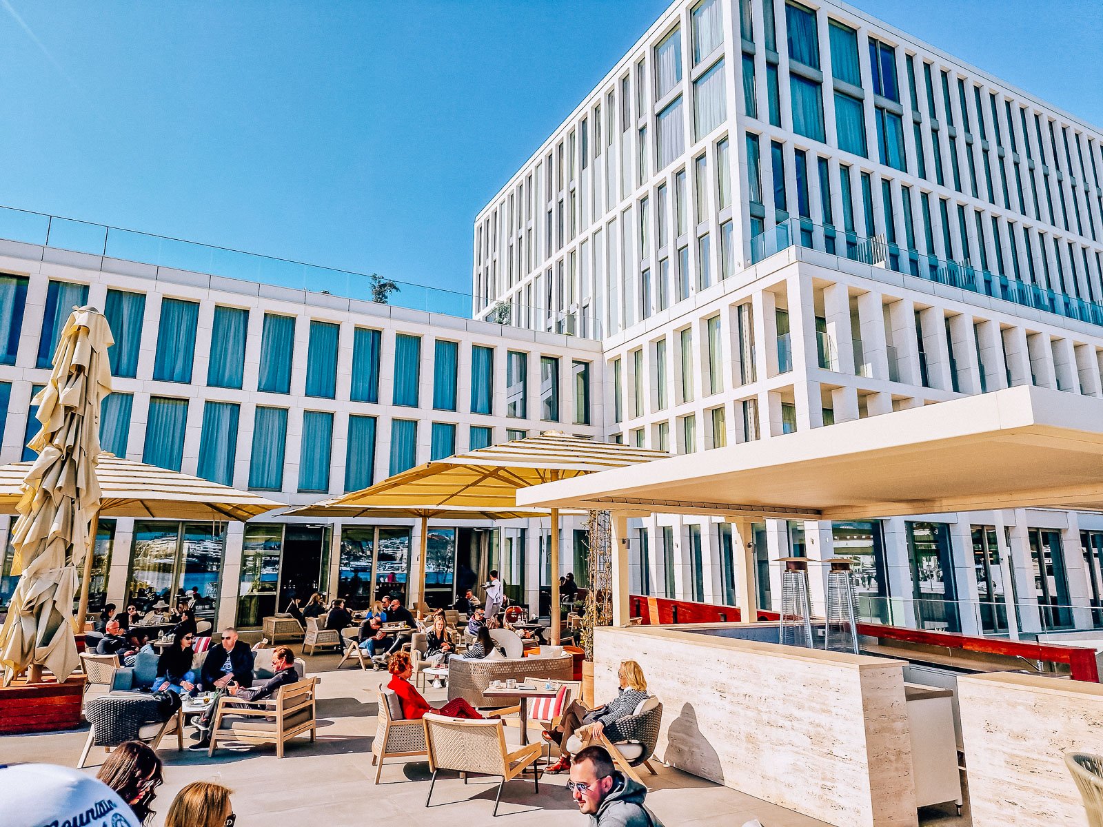 A sun terrace with people enjoying drinks in the sun in front of a modern white building