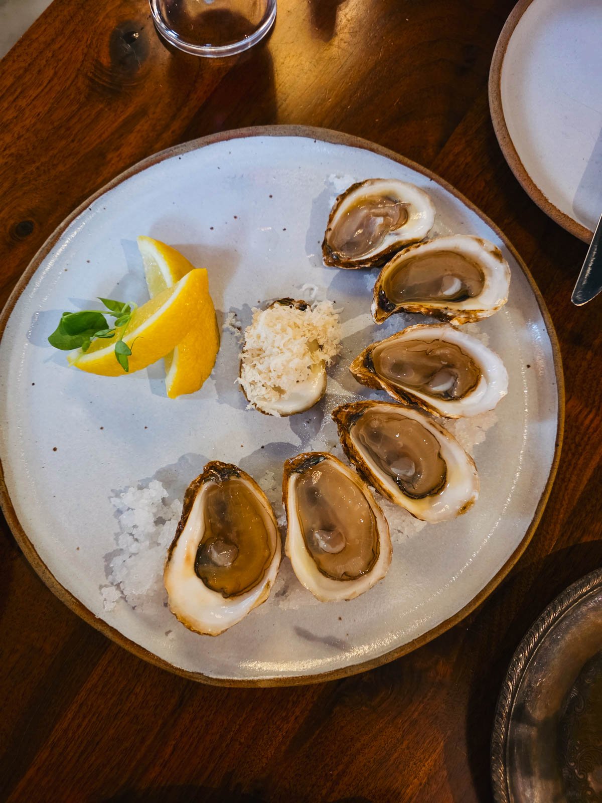 Six Oysters arranged in a half circle on a plate next to two slices of lemon