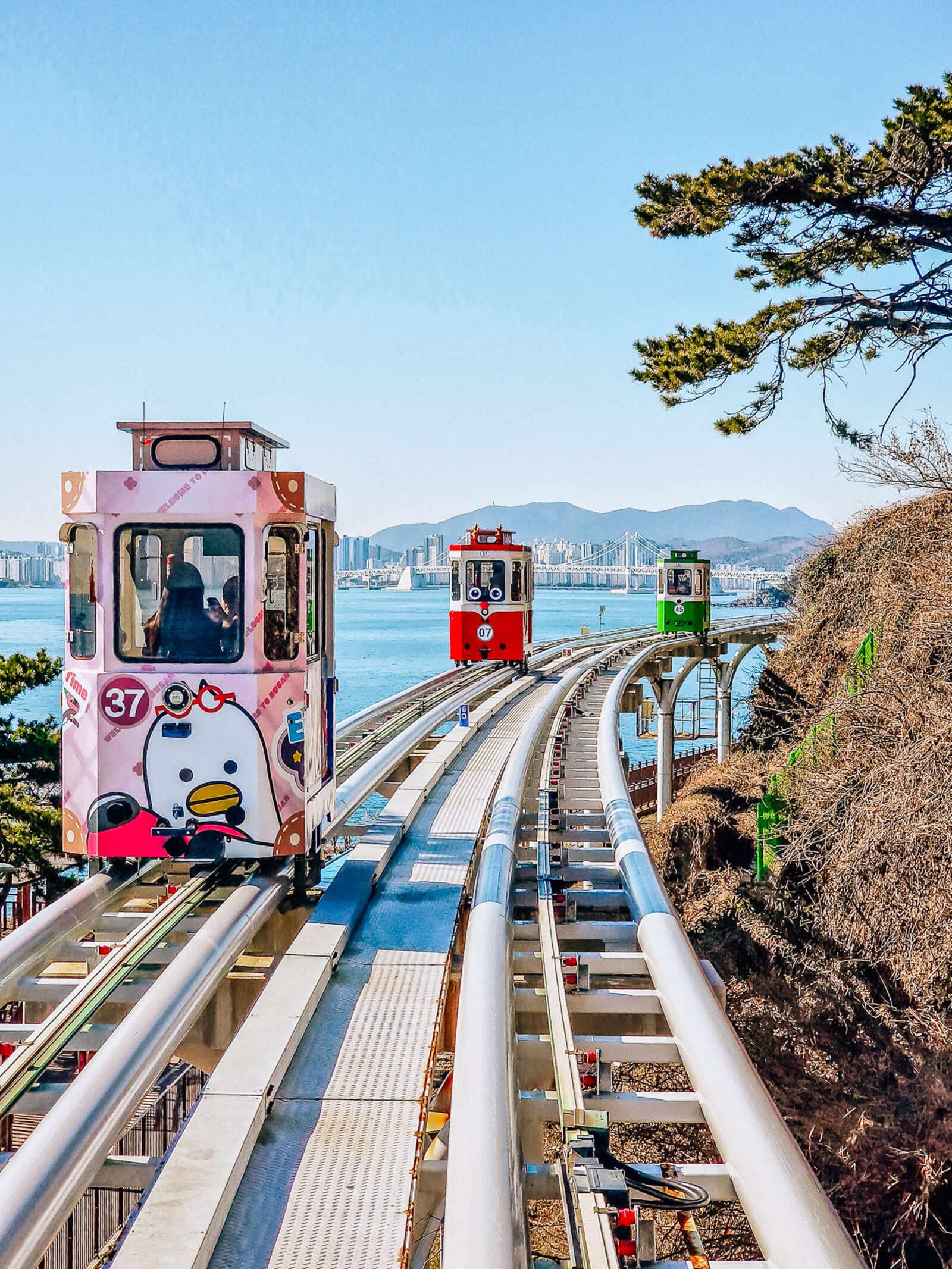 a raised track with 3 capsules running along the track like cable cards. Views of the sea and city beyond