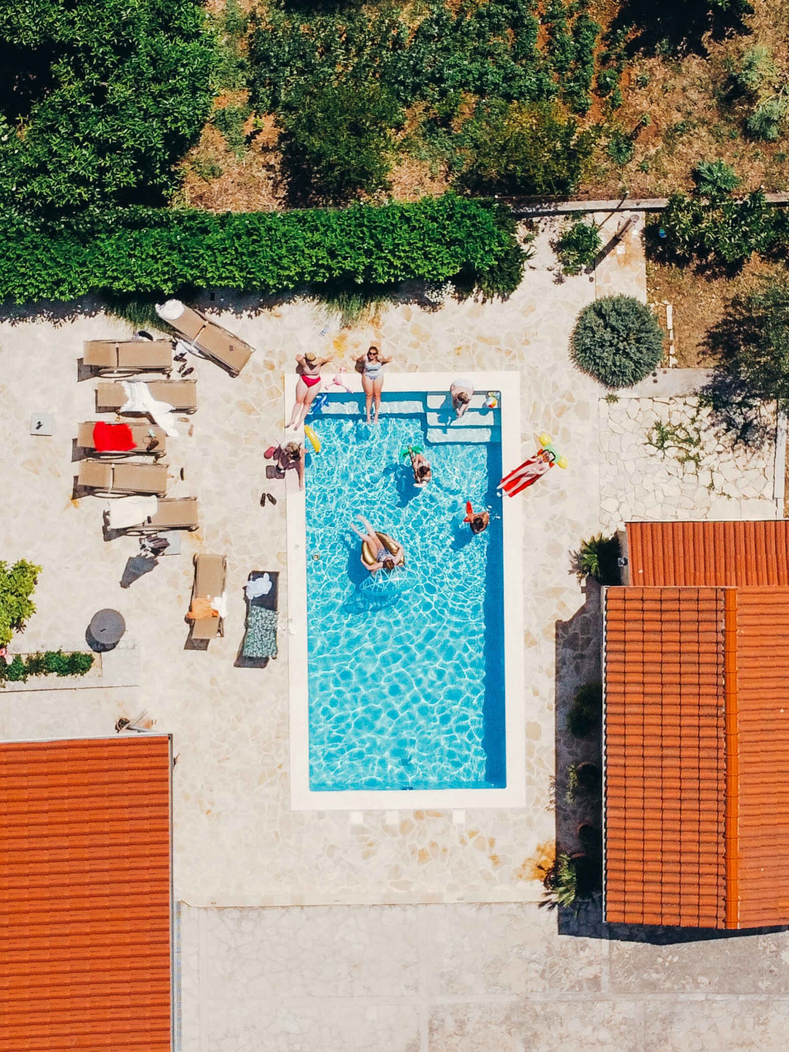 A drone shot looking down on a group of girls floating in and sitting aorund a rectangular pool