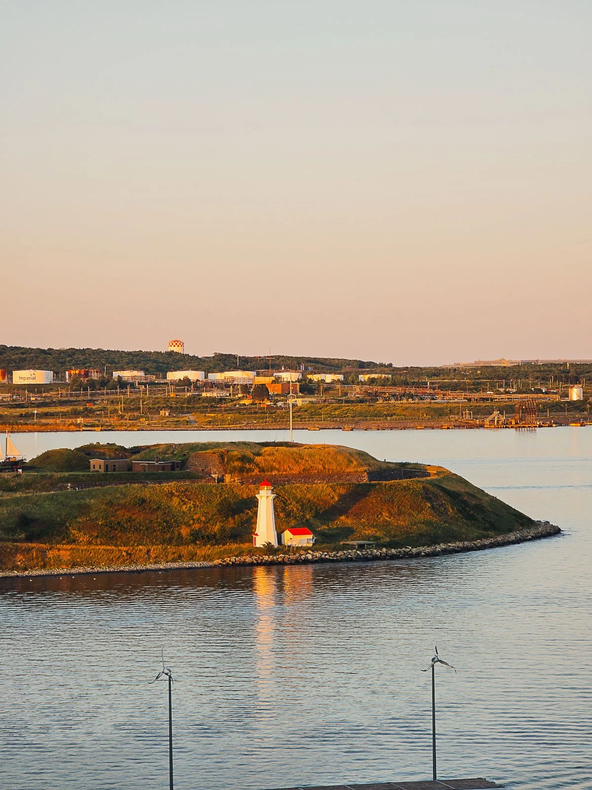 A view of a small island with a red and white lighthouse during sunset