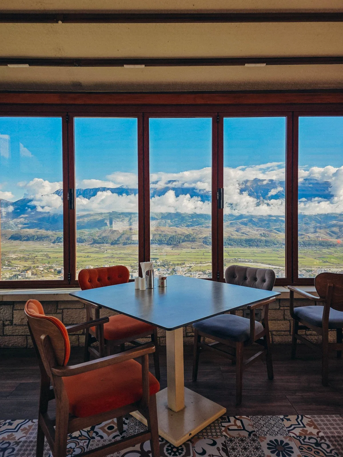 A restaurant interior with a table and chairs next toa large window with a view of large mountains in the distance
