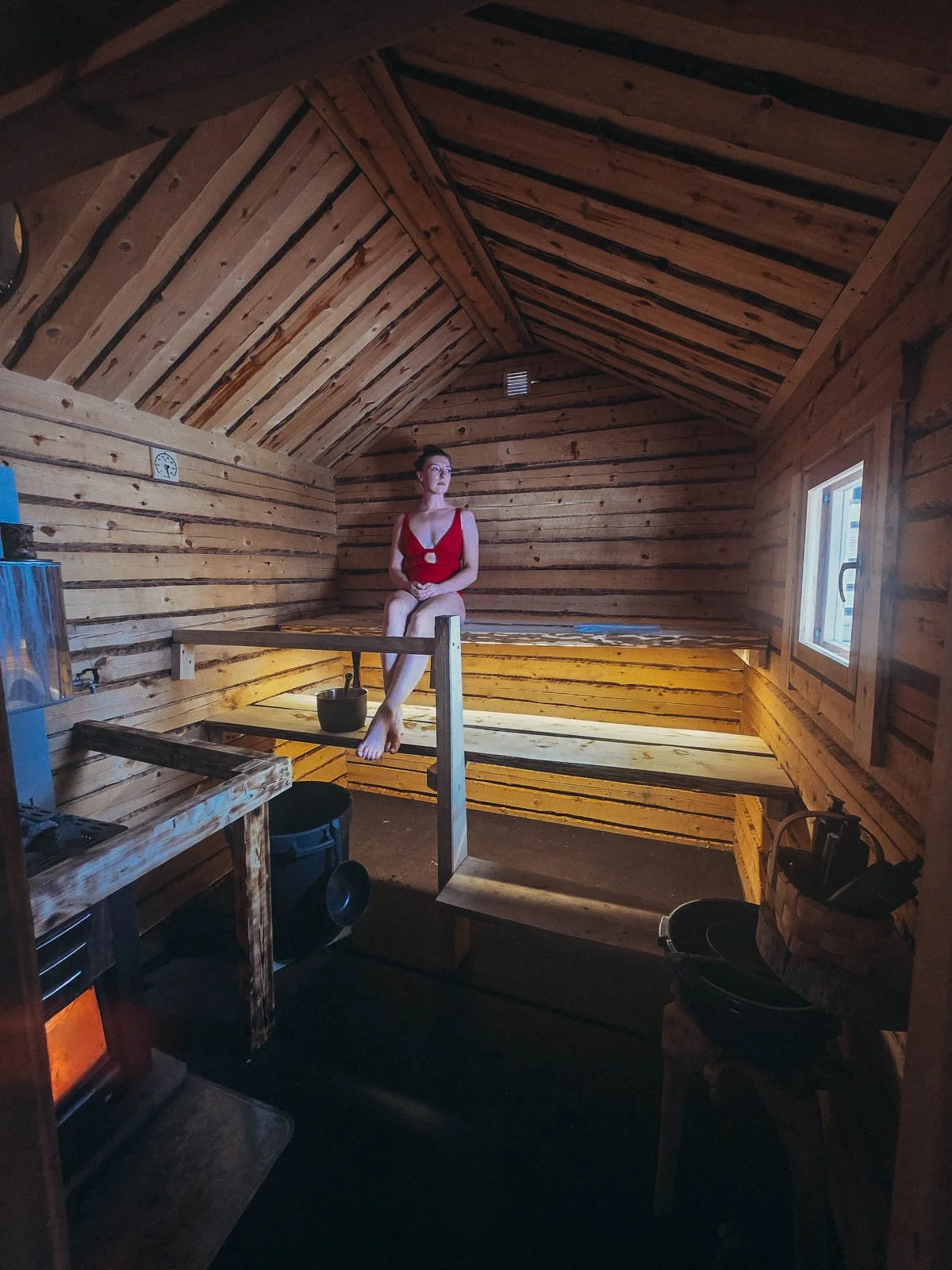 Helena in a red swimsuit sitting on a bench in a small wooden private sauna