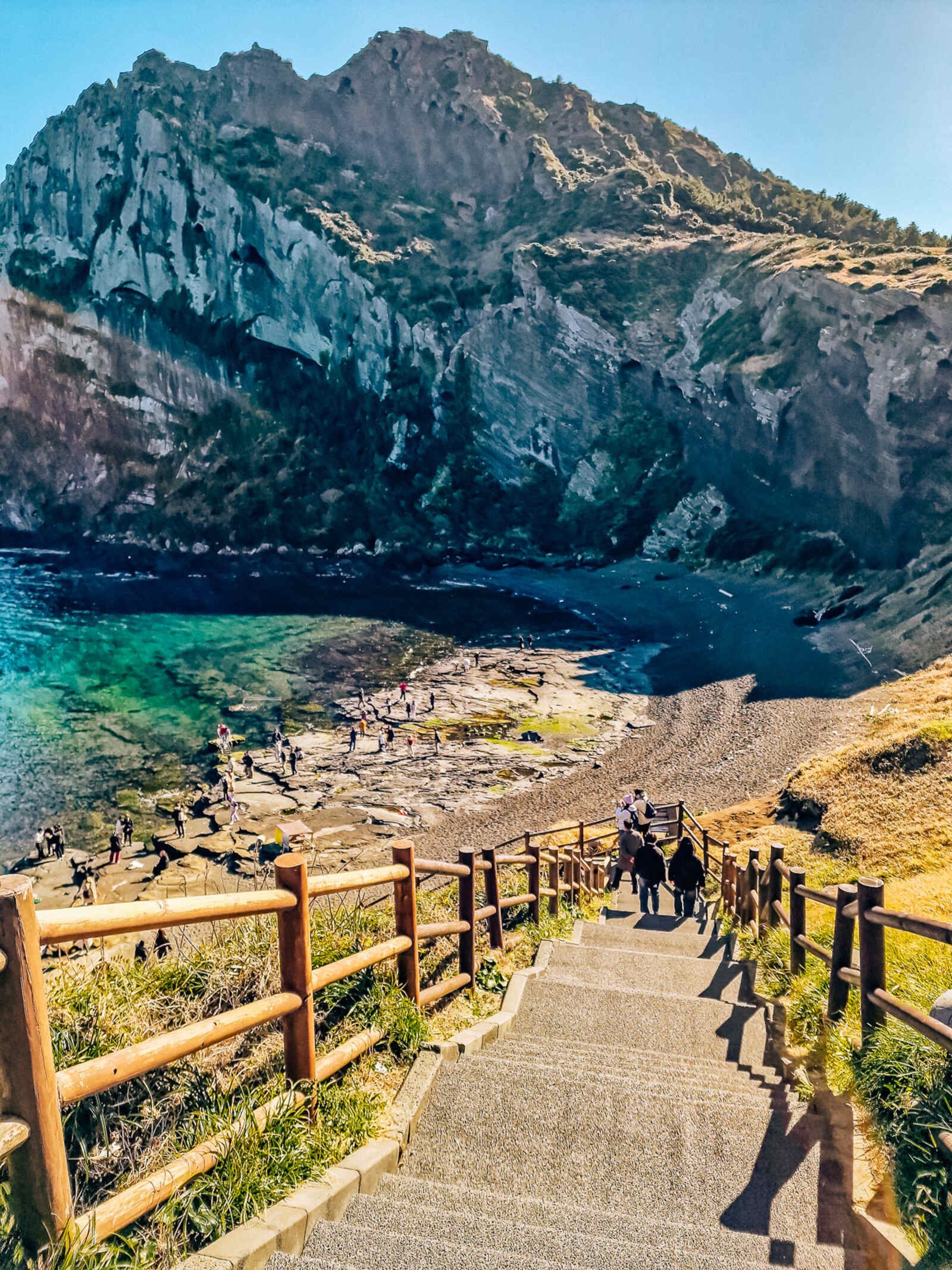 steps leading down to a green bay, partially shadowed by a huge cliff