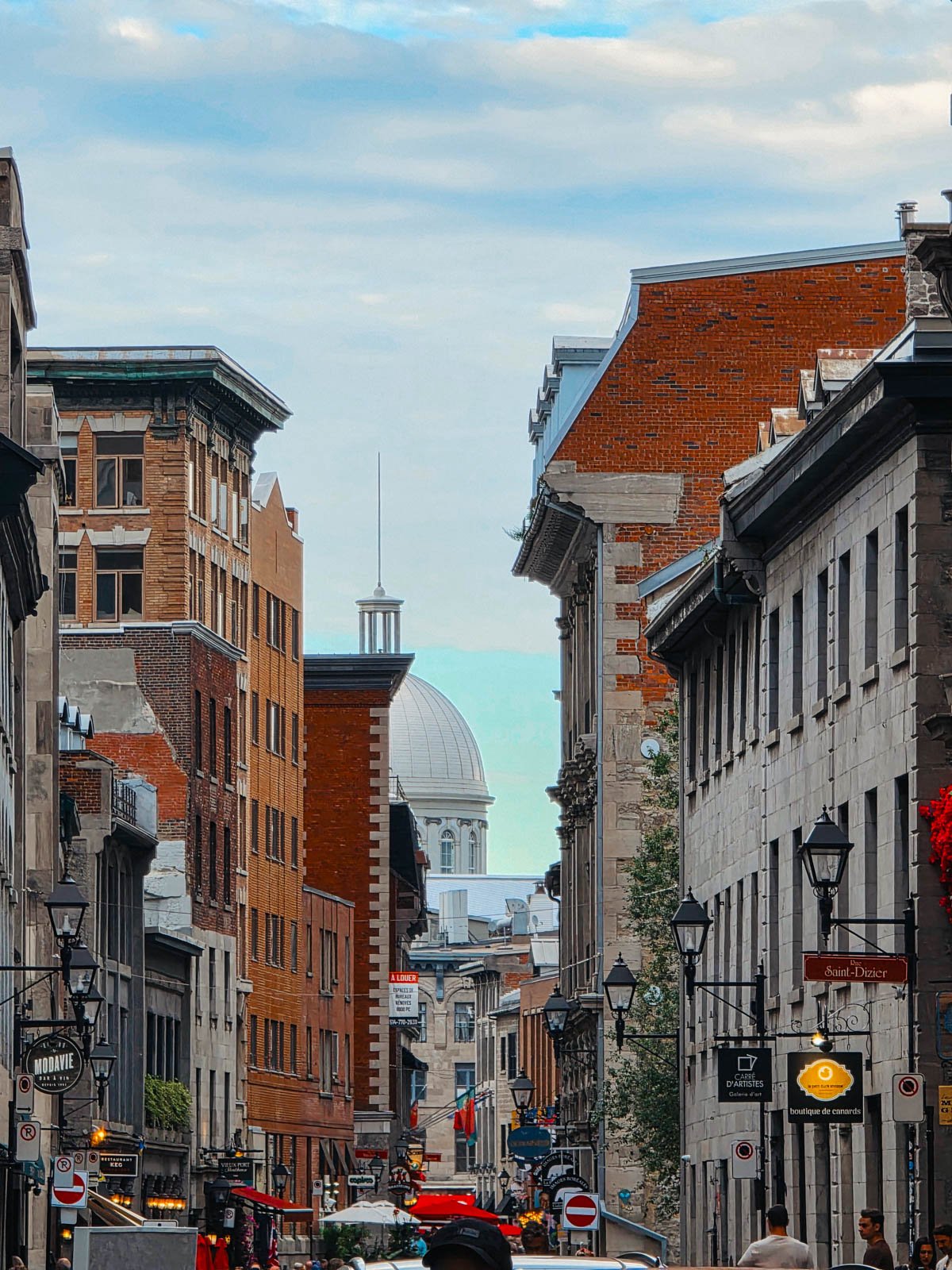 Looking down a busy street in Old Montréal  with lots of old stone buildings and brick facades and a silver dome in the distance