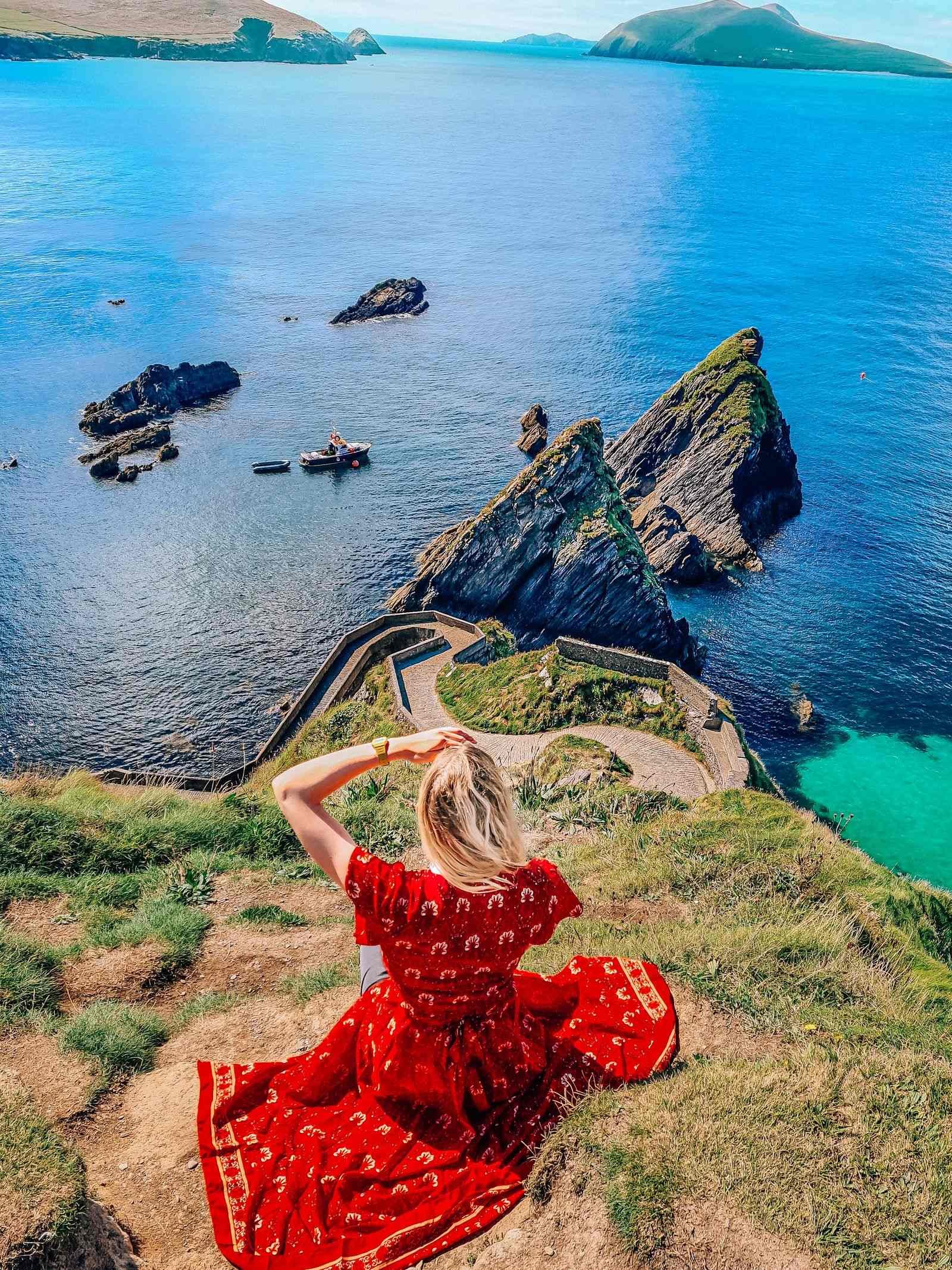 girl in red dress sitting on a cliff above  pier with a view of islands and blue ocean