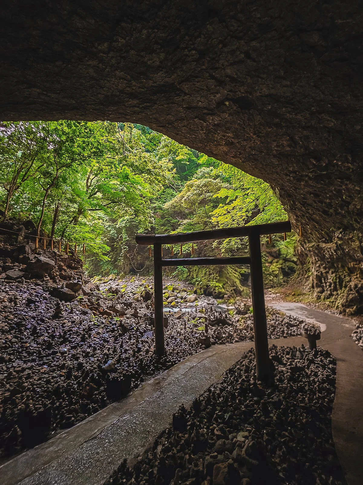 Looking out of a cave opening with a single torii gate sihouetted against the light of the cave opening