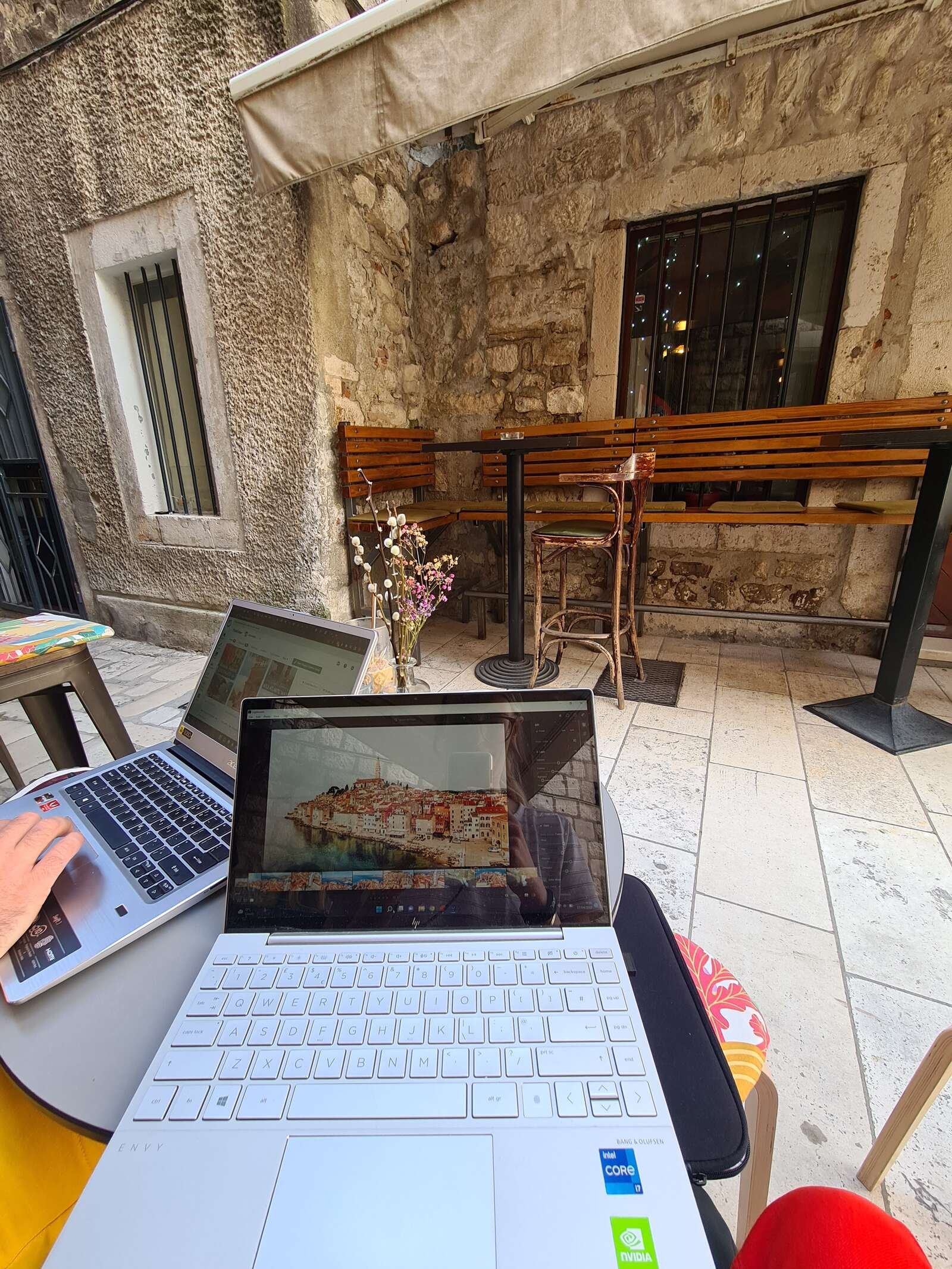 two laptops on a table outside in old town split with old street in the background