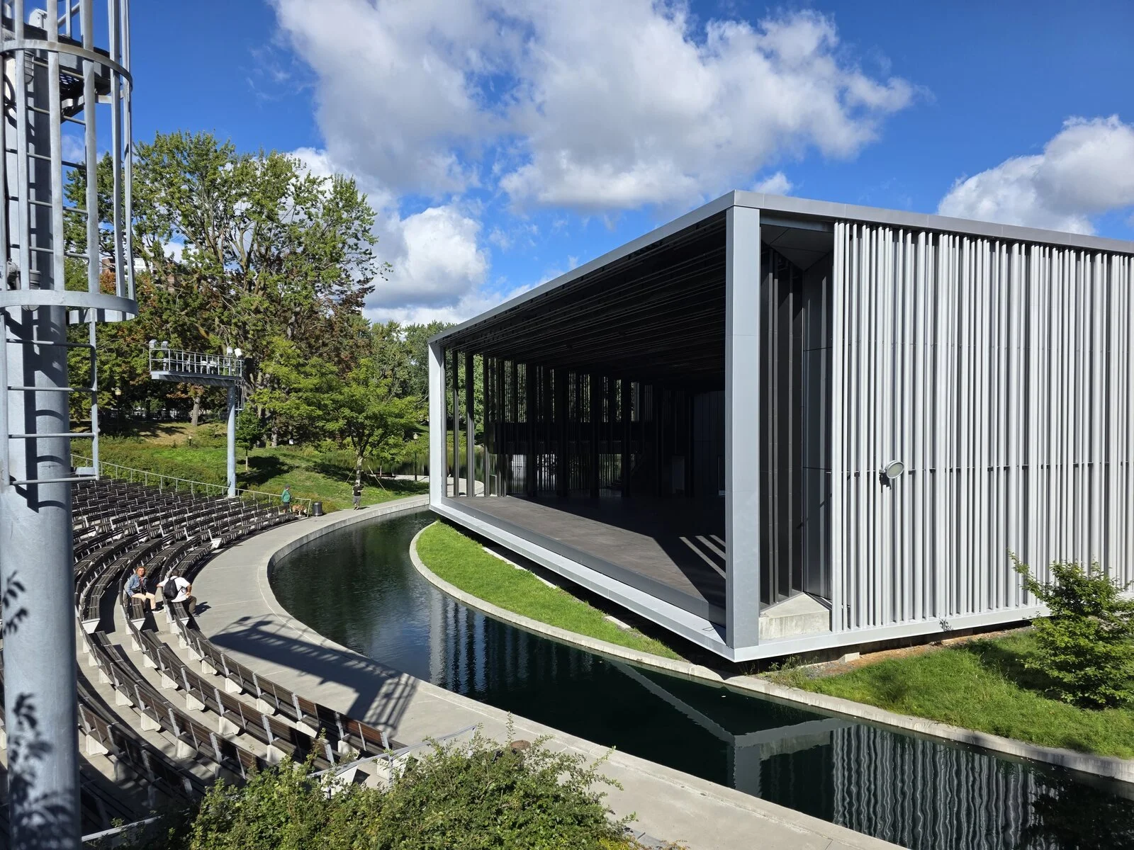 A big outdoor theatre stage surrounded by a river of water and beyond the water is an ampitheatre of seating in a park in Montreal - Théâtre de Verdure