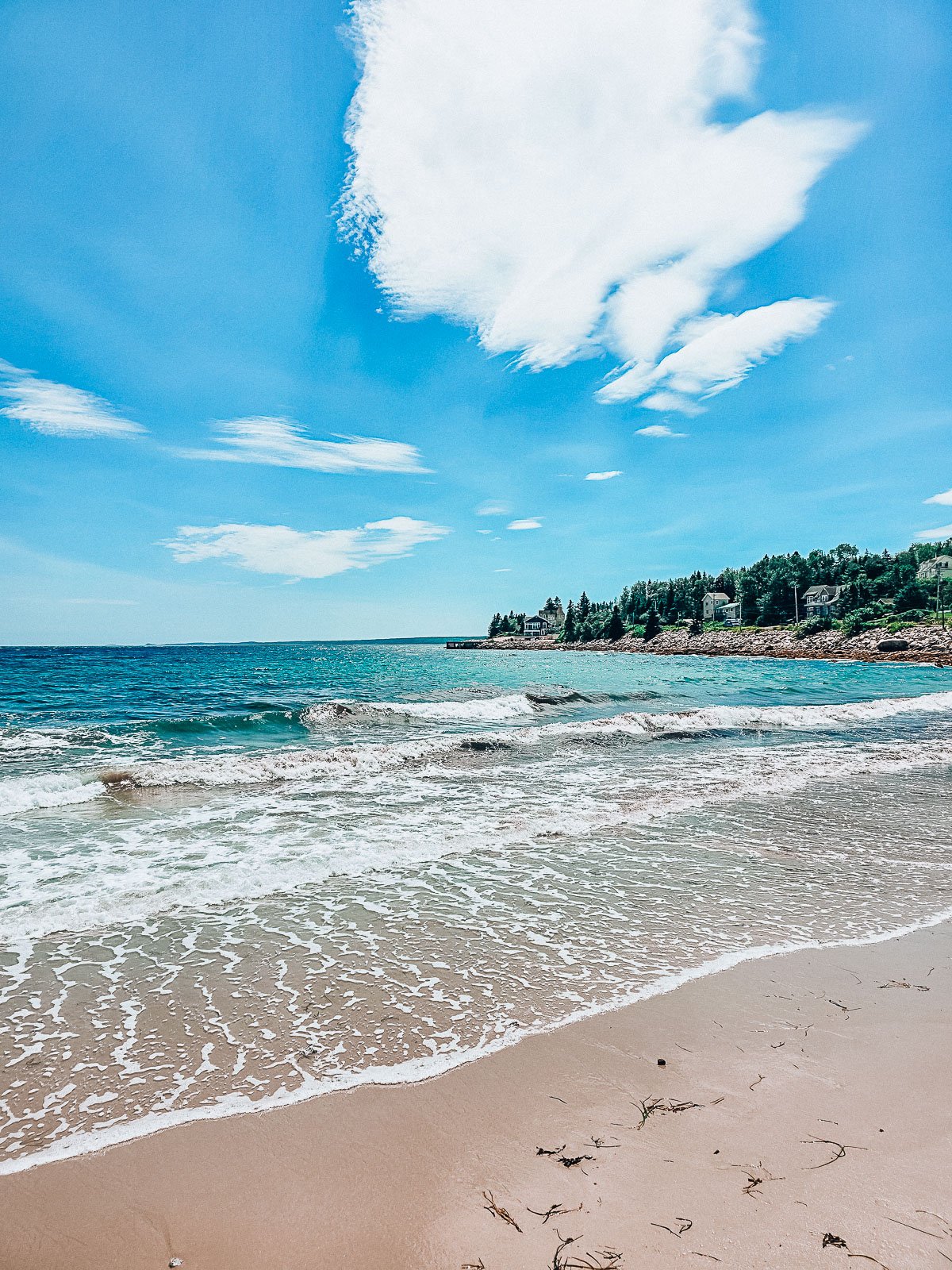 standing on the edge of the shore where small waves are lapping at the sandy beach. Sky and sea are blue