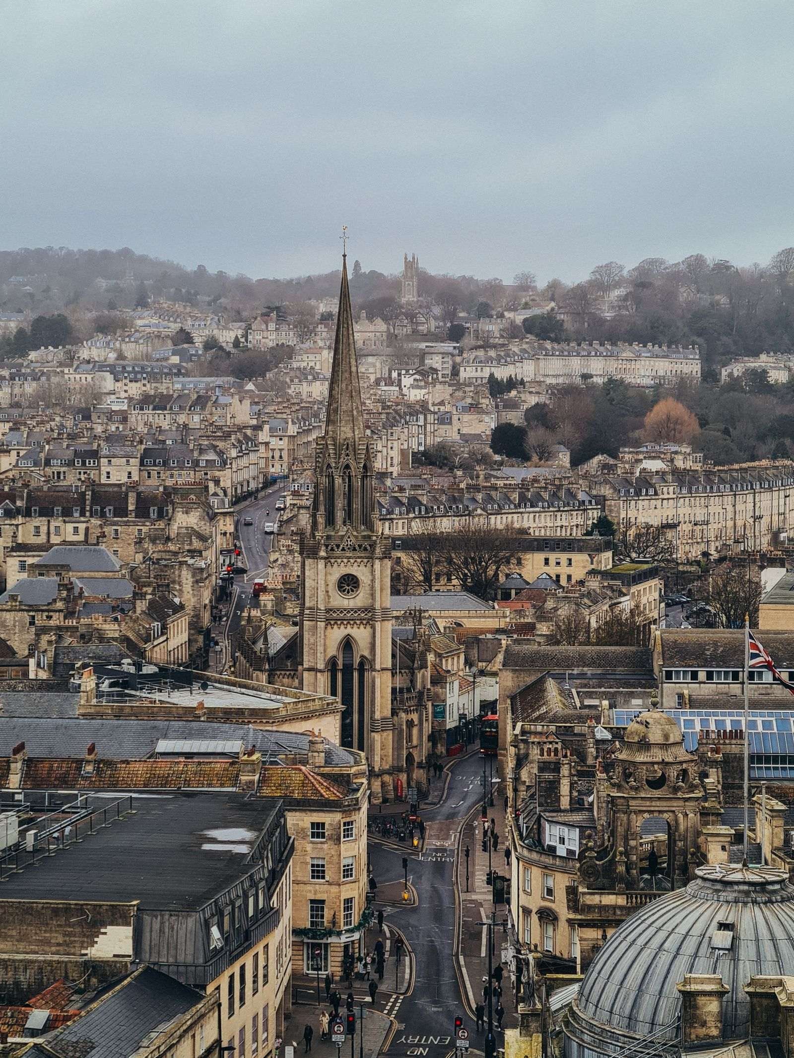 A view looking down onto bath city centre with roads snaking through many stone buildings and a large church in the middle