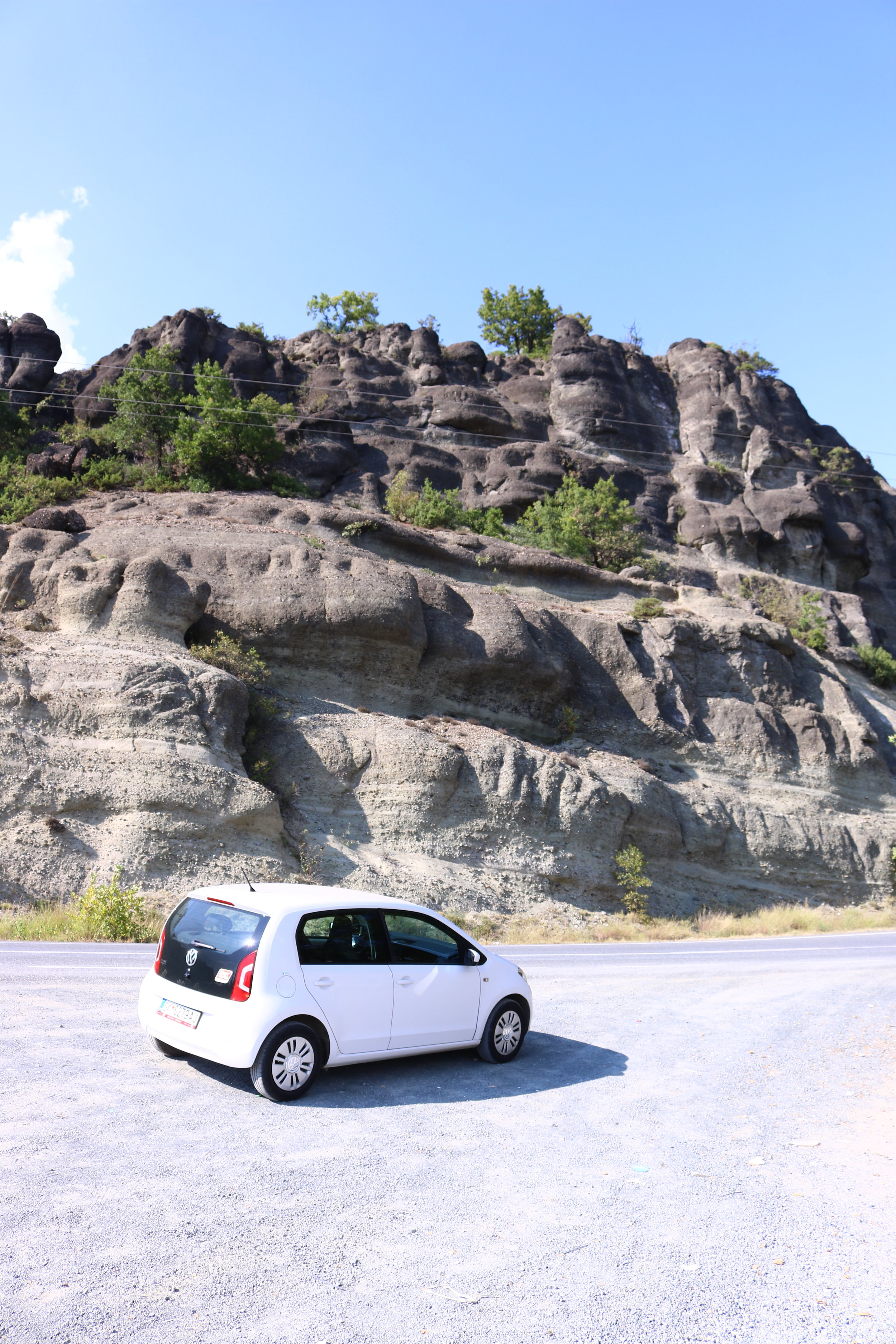 white car on the road in front of a rocky cliff