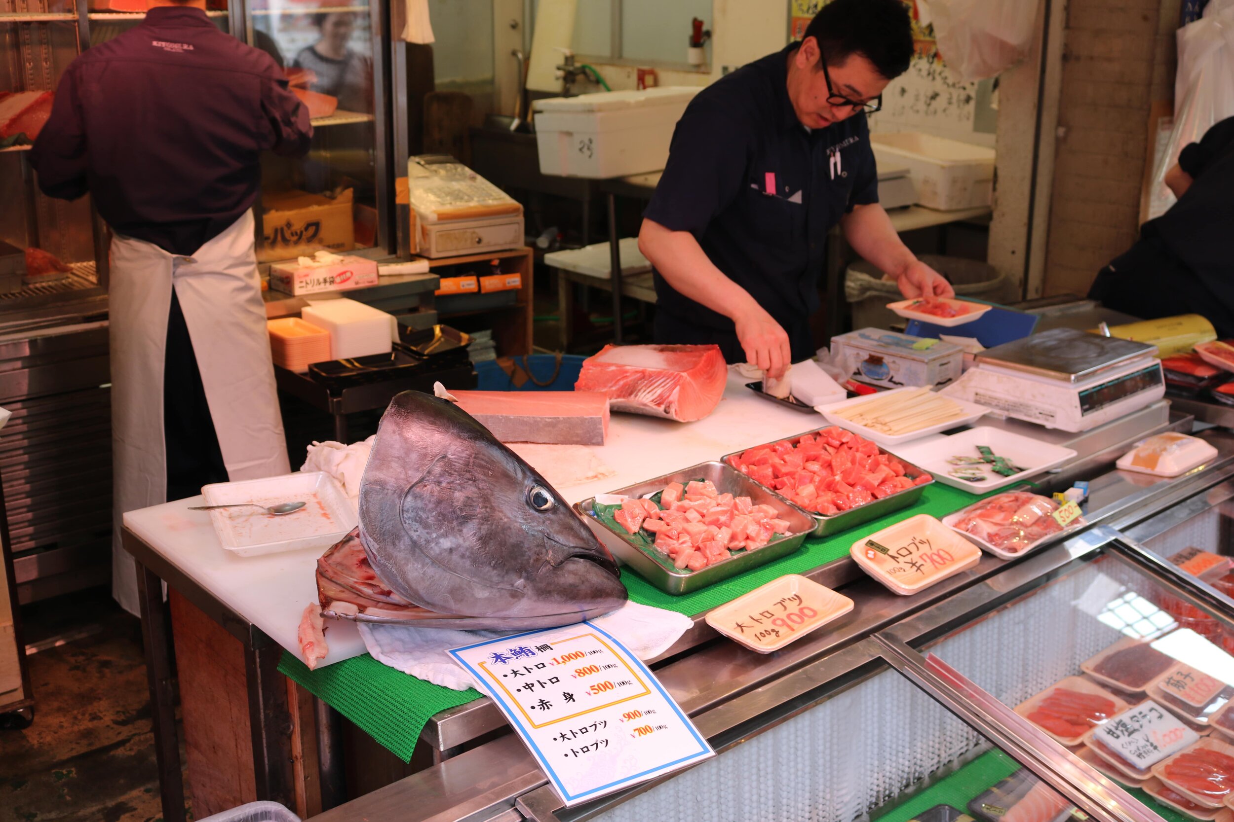 A man at a seafood stall packaging fish with a large fish head on the counter