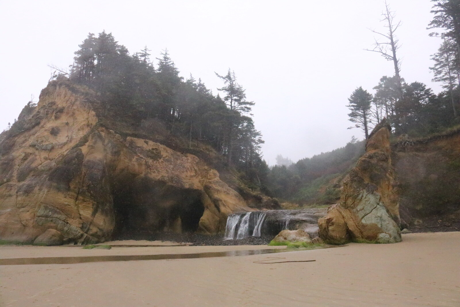 A beach with a small waterfall and cave in the cliffs