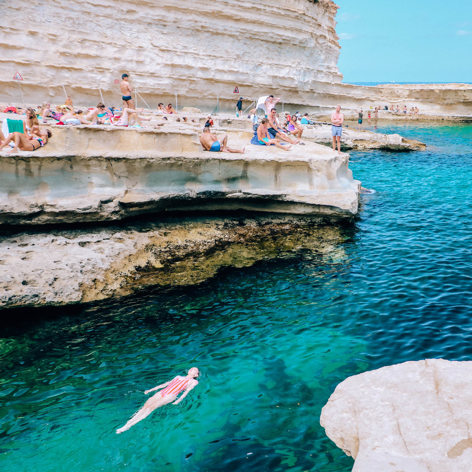 Helea floating in the blue waters of St Peter’s Pool, Malta surrounded by white rocky cliffs