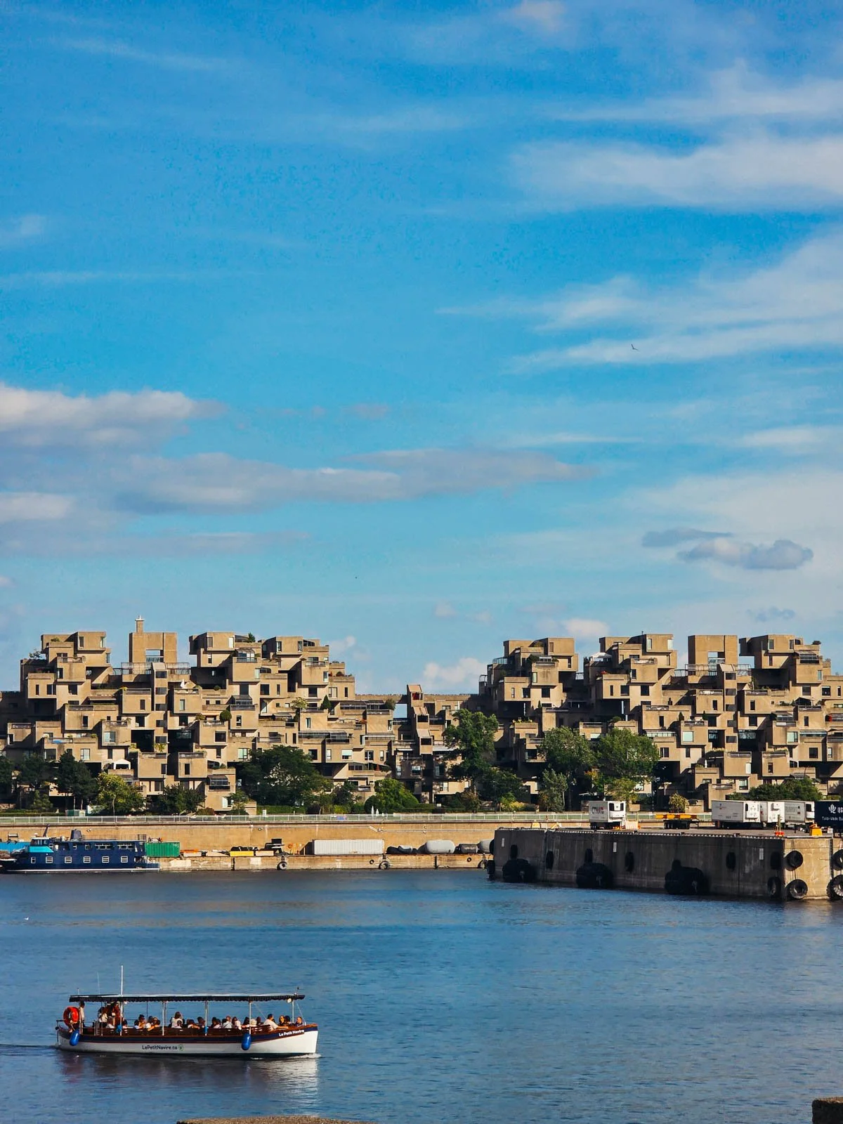 A small wooden boat cruising on calm water in front of the iconic Habitat 67 building in Montreal