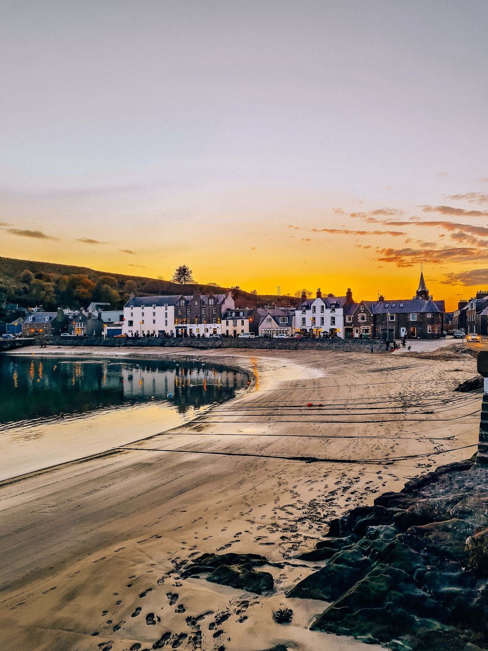 The beach and calm sea in Stonehaven harbour, Scotland at sunset with white cottages on the far side of the harbour