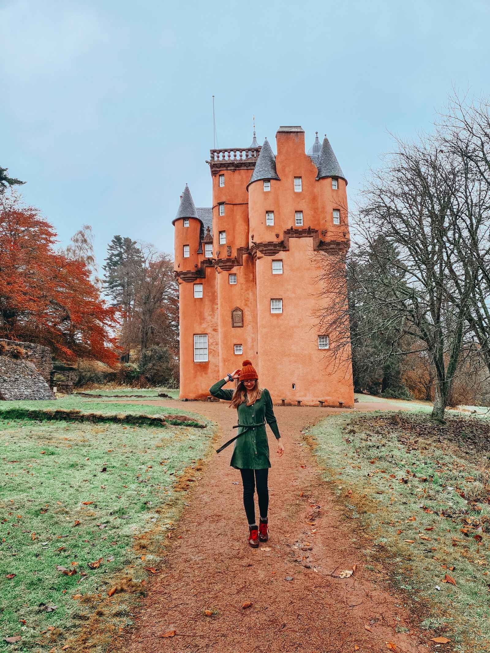 Woman in a green dress walking down a path in front of a large pink castle, Craigievar Castle