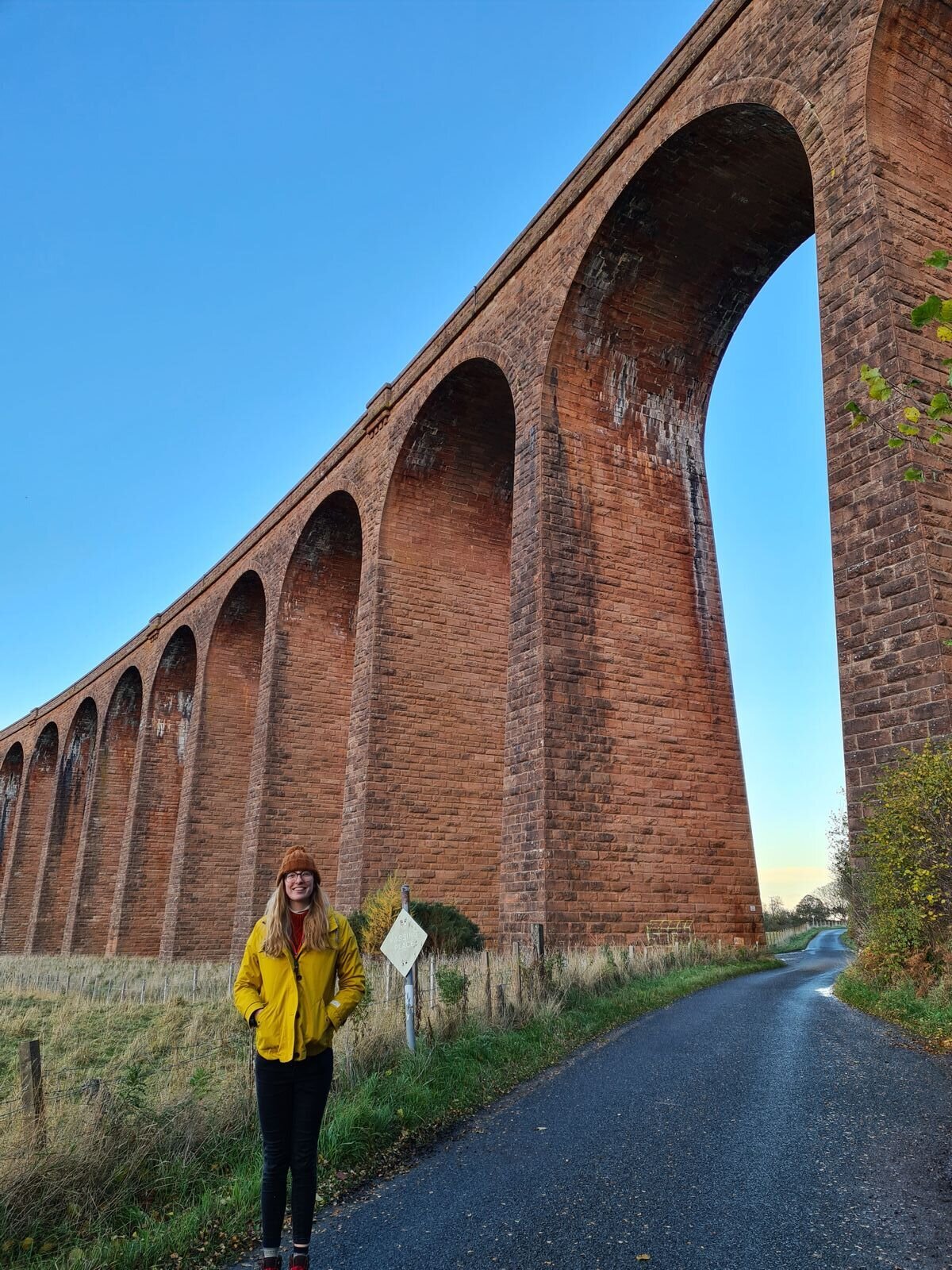 Nairn Viaduct, a large red brick stone viaduct looked at from below with a woman in a yellow jacket standing beneath it