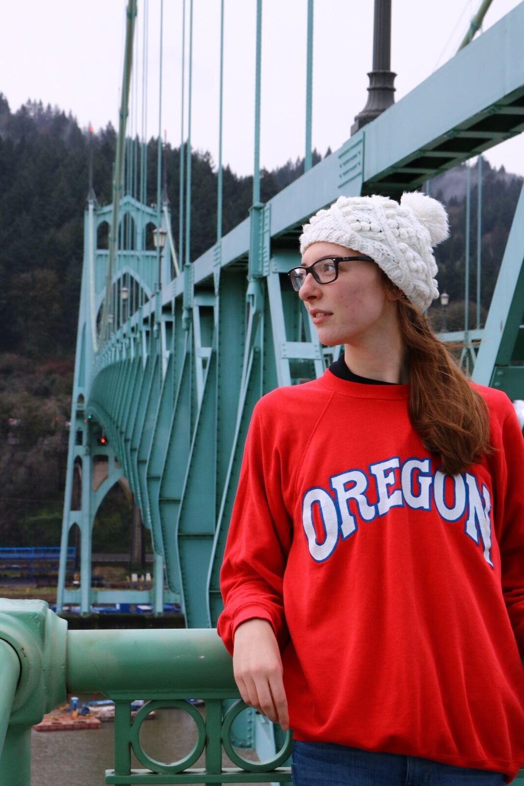 Helena in a red sweater standing in front of a large green St Johns Bridge