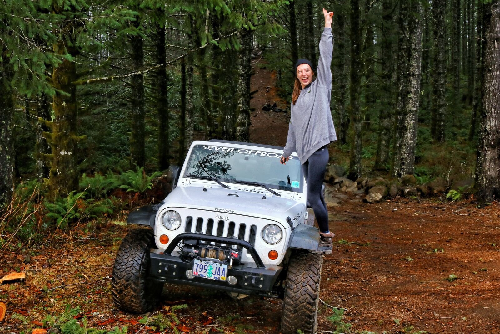 Helena standing on the tires of a large white jeep while off-roading in Oregon