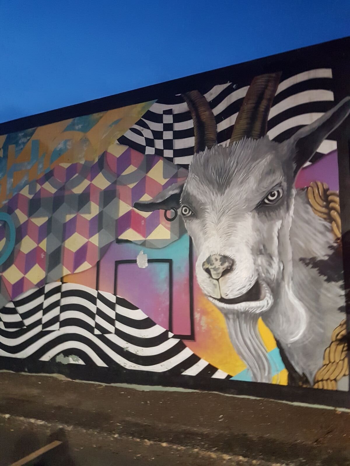 A large goat pained on the side of a building with many colors surrounding it. Portland street art