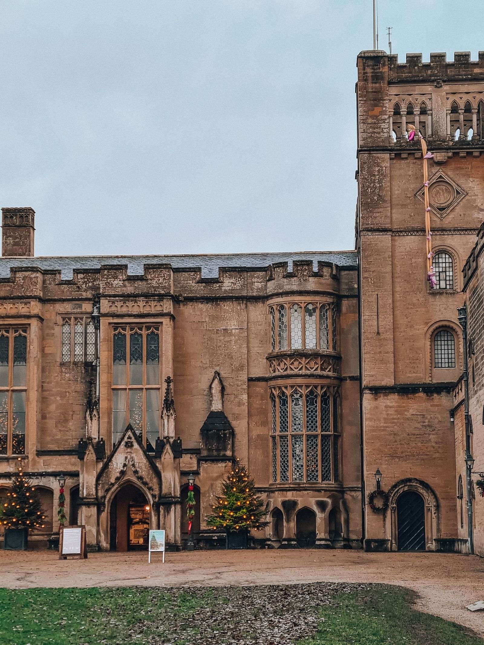 A grand entrance to a large sandstone building with turrets and large windows. Main porch is flanked by two christmas trees - Newstead Abbey