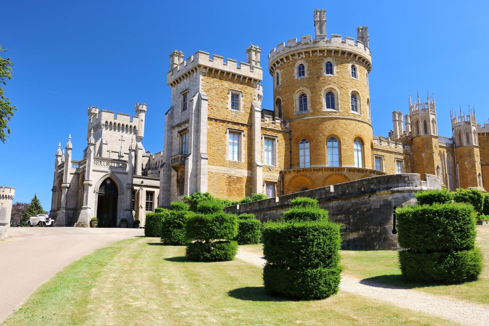 a sandy coloured castle with turrets and many windows. Landscaped gardens in front