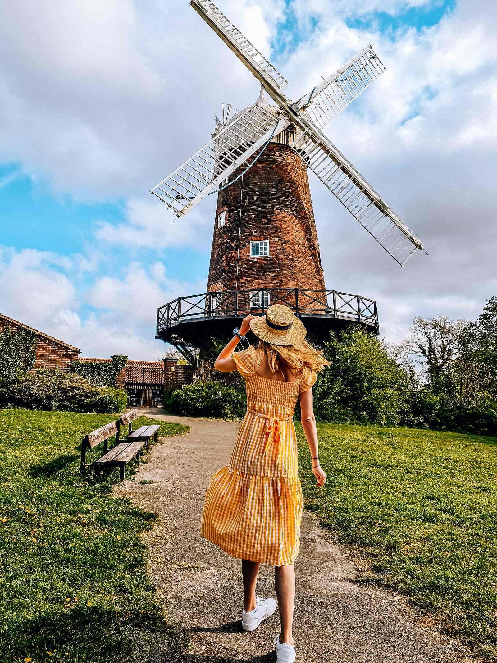 A girl in a yellow dress standing on a pathway with a old brick windmill in the distance