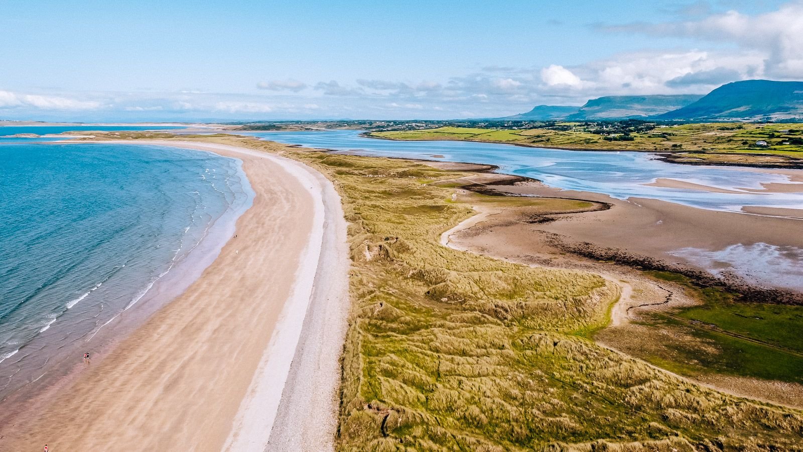 drone image of a sand bar beach with mountains in the background