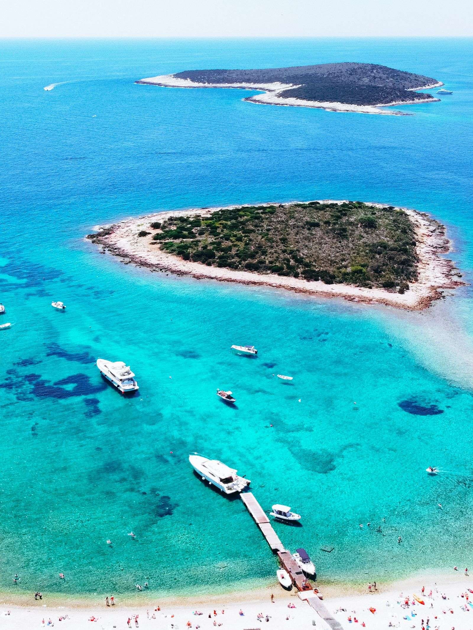 an aerial photo of a vivid blue lagoon with a heart shaped island covered in trees and small white boats in the turquoise water