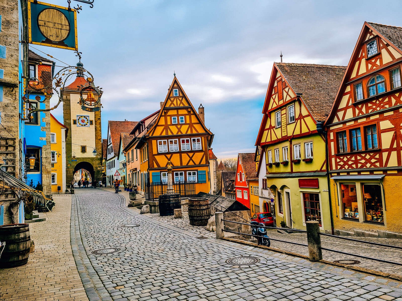  A cobbled street running many colourful traditional German buildings. One building is Orange and the other is yellow. 